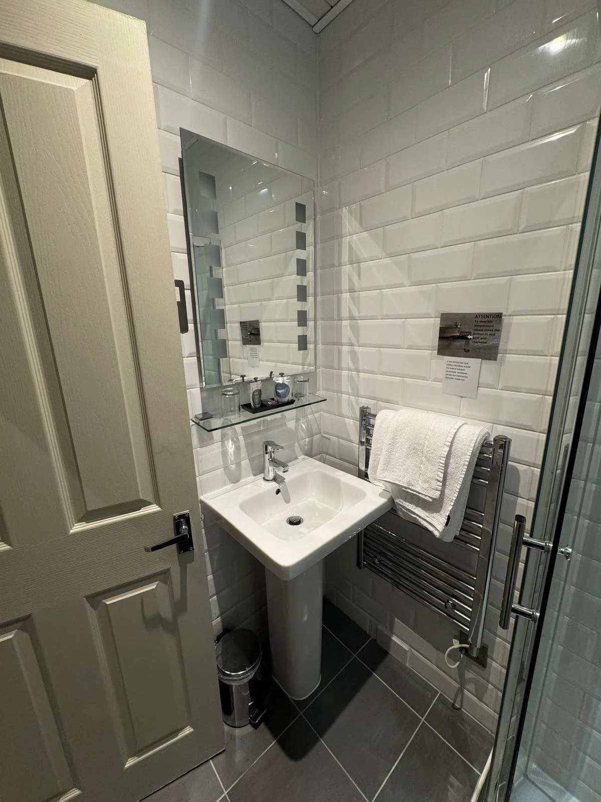 Small restroom with white subway tiles, a pedestal sink, a rectangular mirror, a towel rack with a white towel, and a glass shower door.