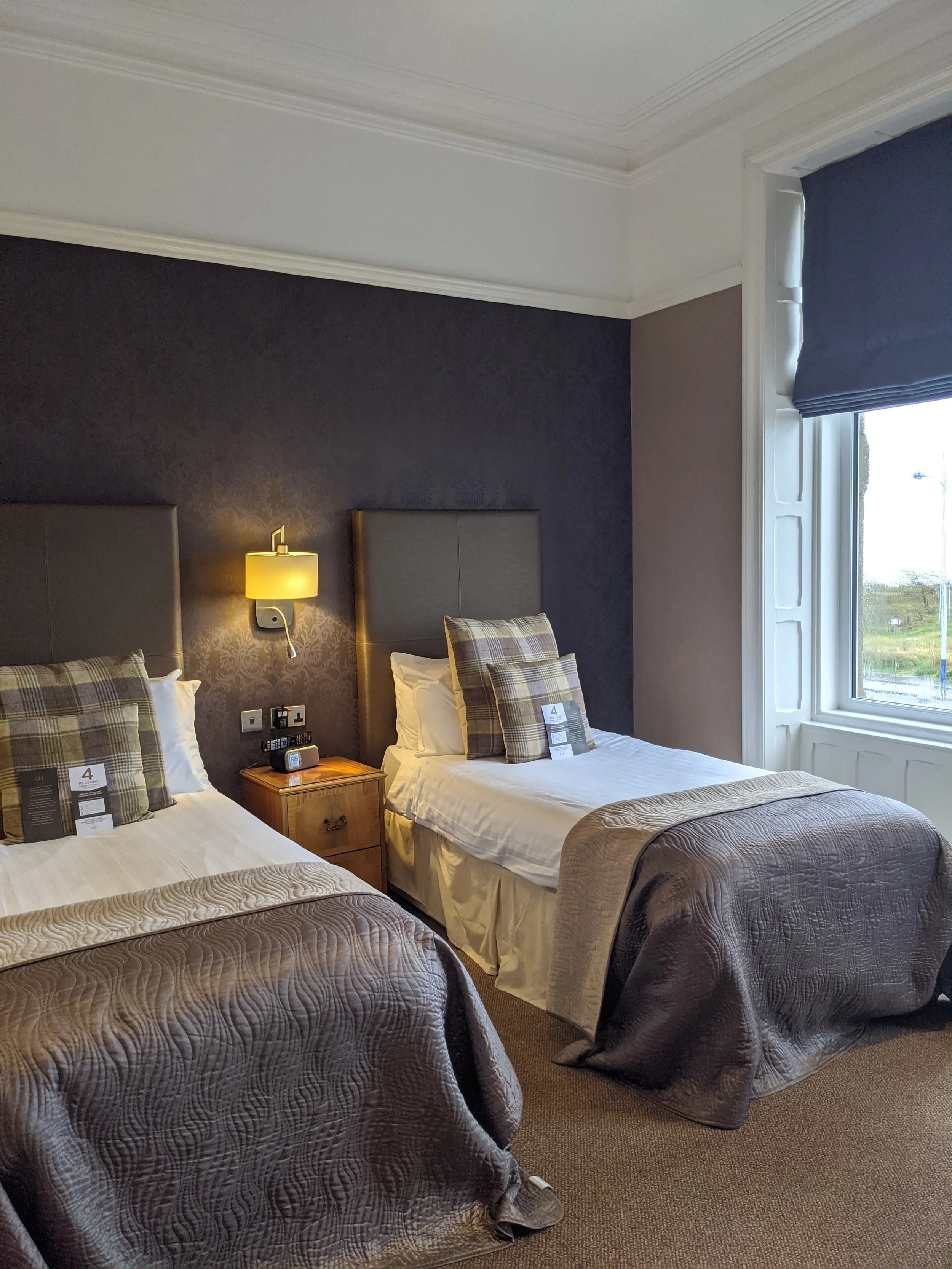 Hotel room with two twin beds, a bedside table, and a window with a blue curtain.