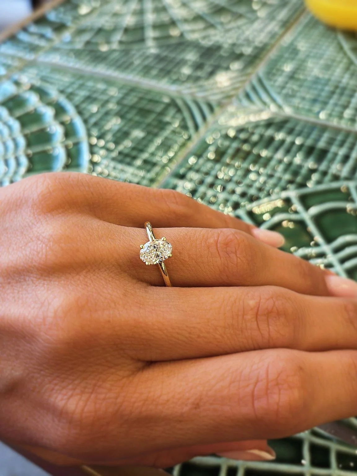 A hand wearing a gold ring with a large cluster of diamonds against a background of green leaves.
