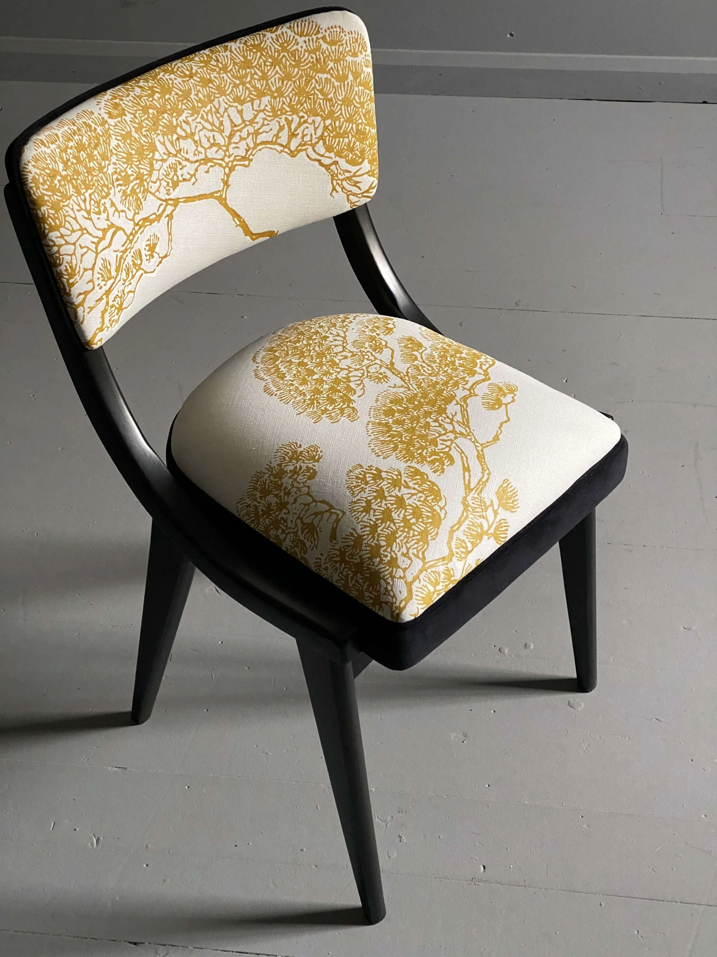A black wooden chair with a white upholstered seat and backrest, both featuring a yellow intricate tree branch pattern.