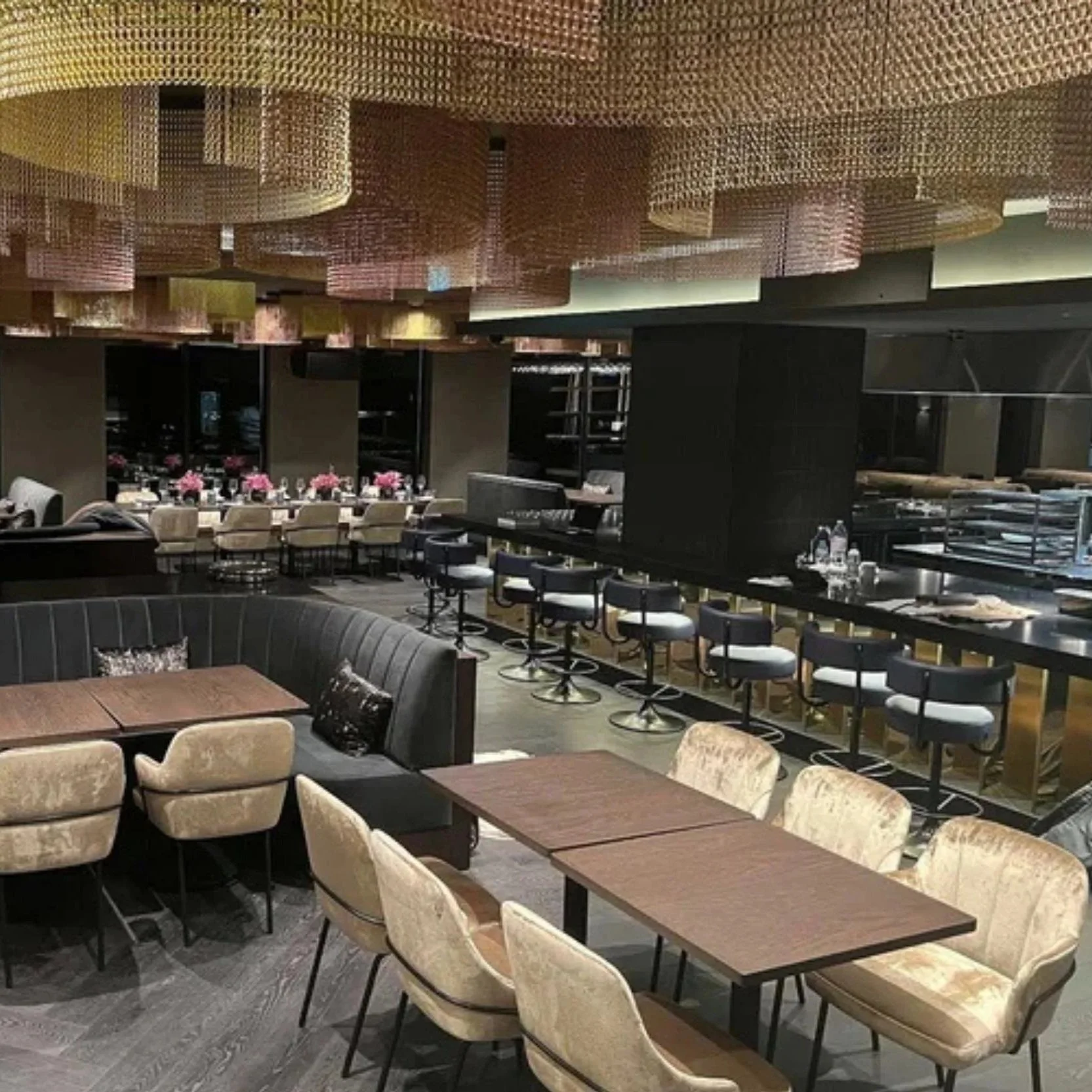 Interior of a modern restaurant with various dining areas, including a bar with stools and multiple tables with chairs, decorated with pink flowers.
