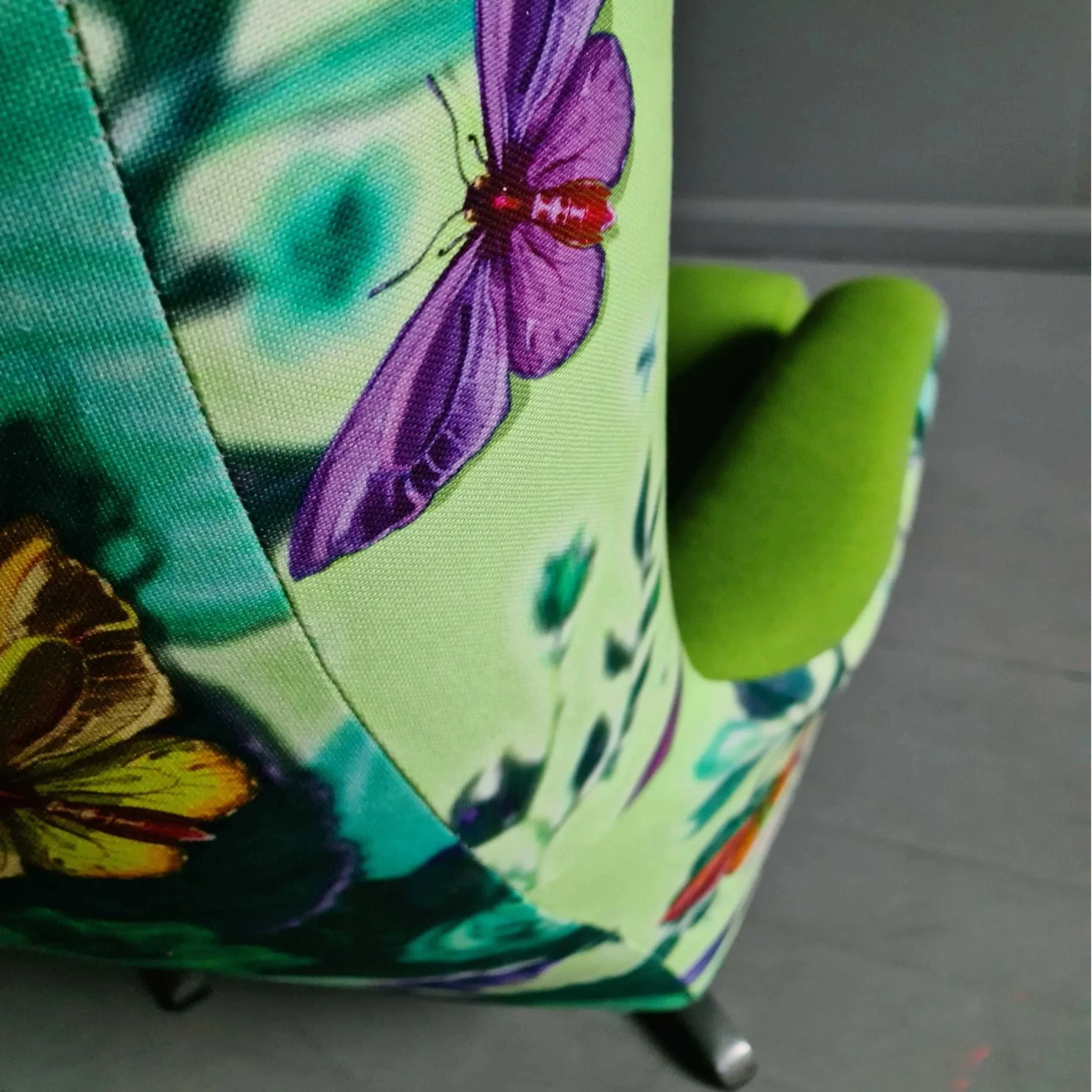 Close-up of a colorful fabric with butterfly and insect designs, part of a small piece of furniture with green and black legs.