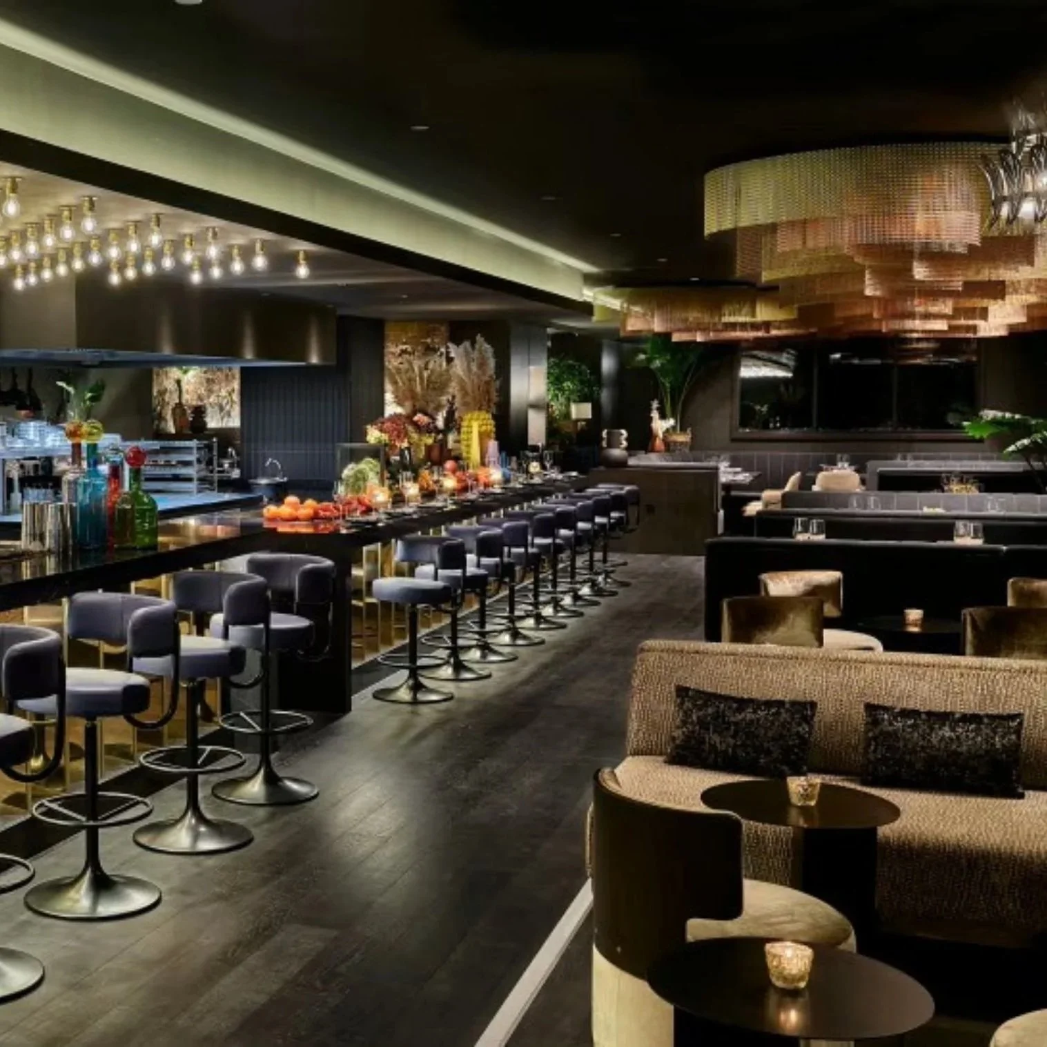 An upscale bar and lounge area with a long bar counter, barstools, and a variety of snacks and drinks on display. Elegant furniture, and decorative lighting fixtures enhance the interior ambiance.