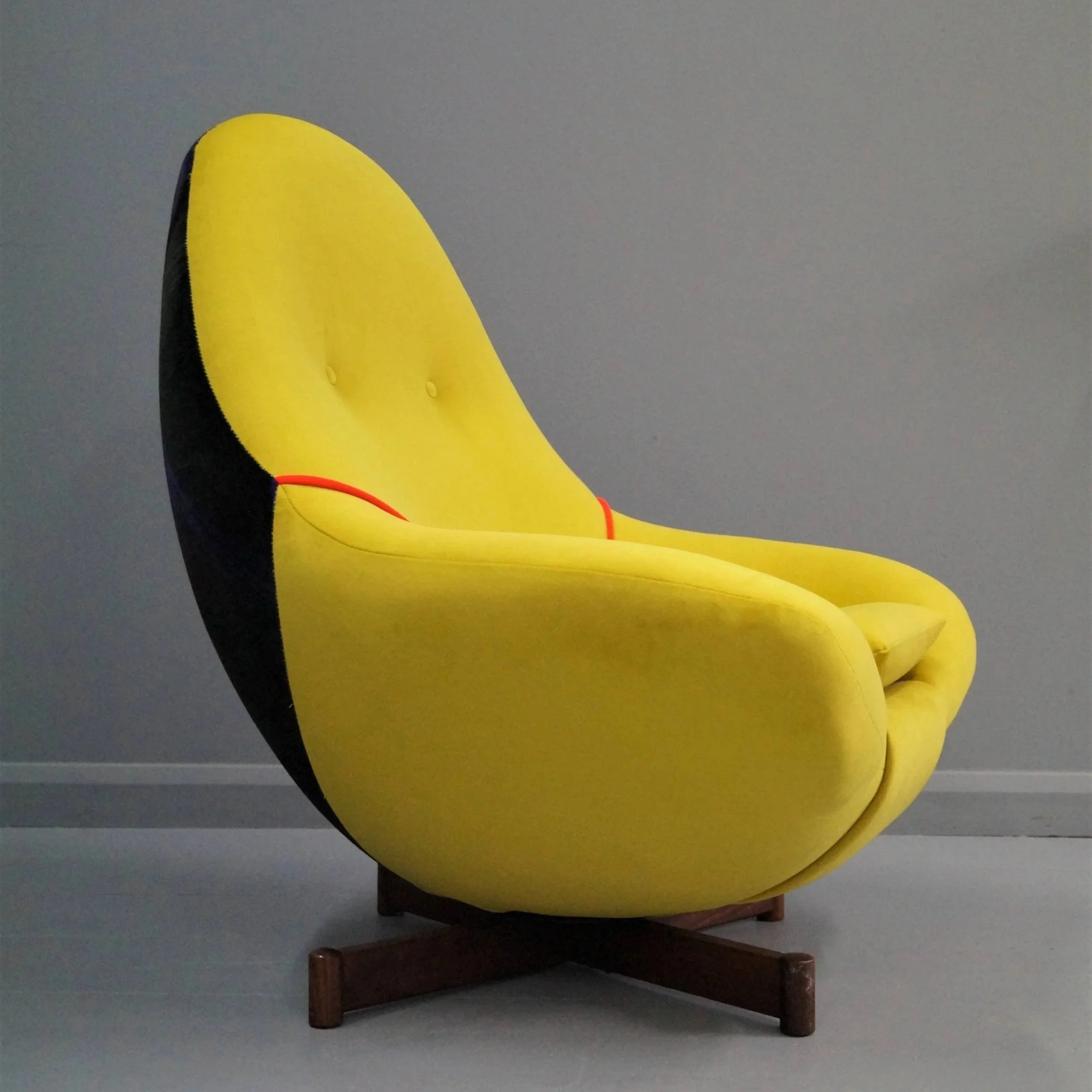 A modern yellow and black egg-shaped chair with wooden legs against a gray wall.