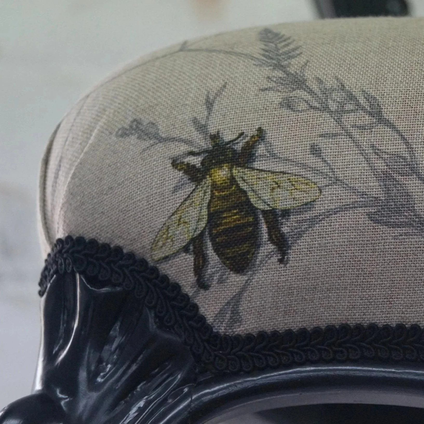Close-up of a seashell with a bee illustration and some botanical artwork, sitting on a black ornate surface.