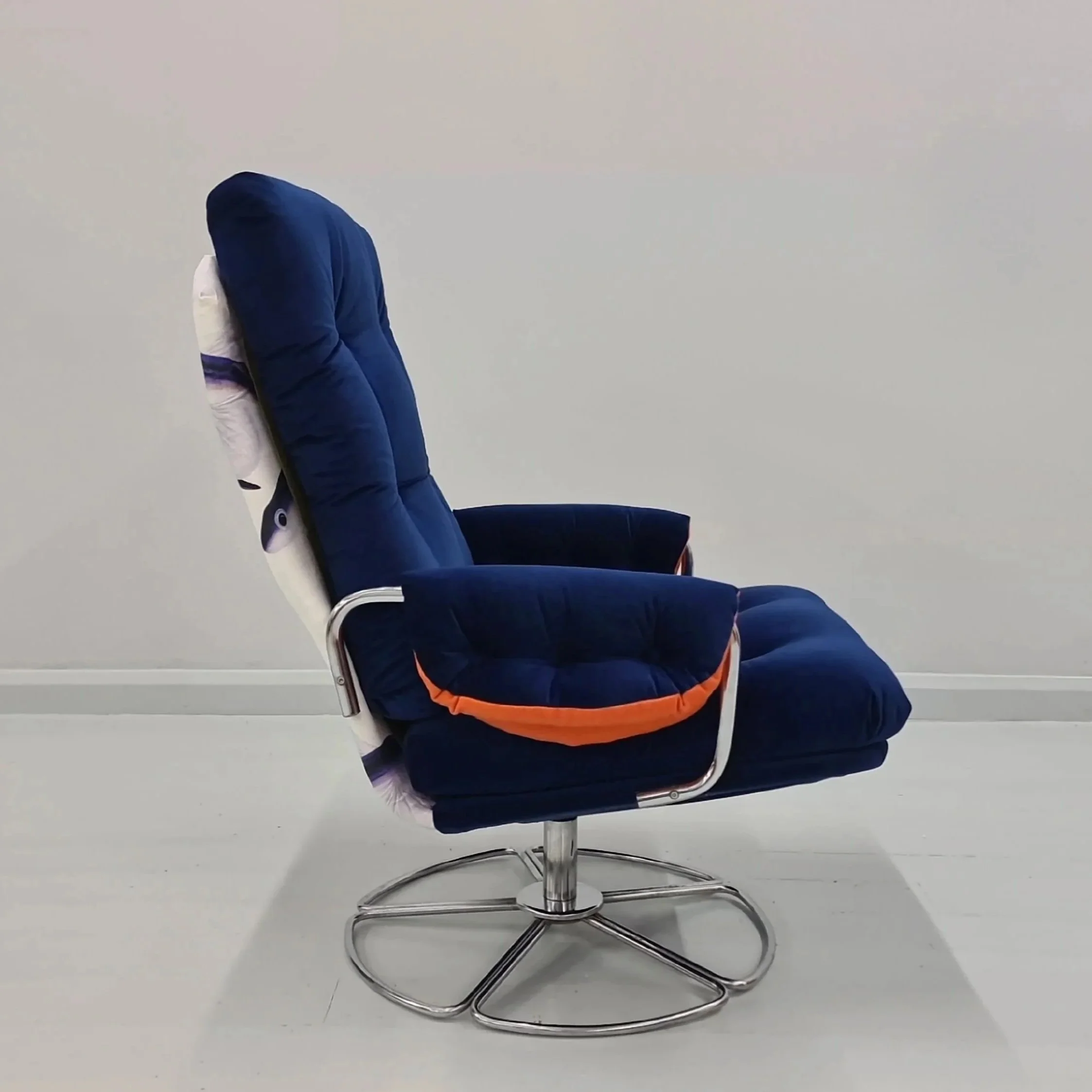 An office chair with a plush, dark blue cushion covering the backrest and seat, with a white and black patterned fabric visible at the side, against a plain white wall and floor.