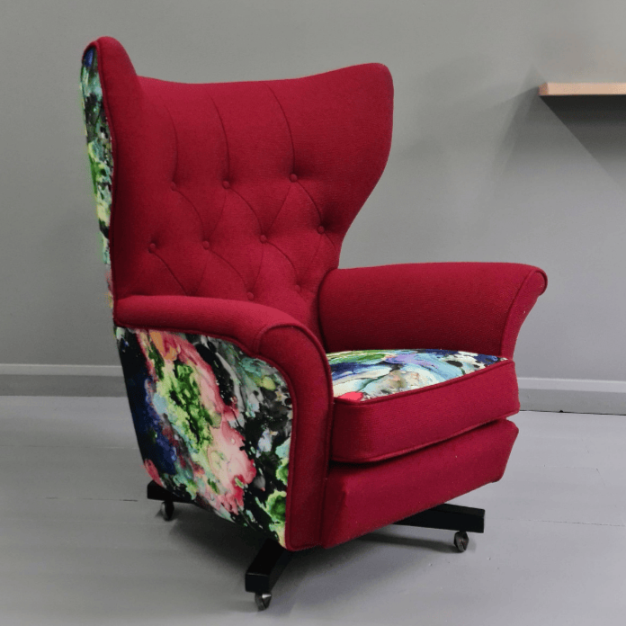 A red armchair with tufted backrest and floral fabric on the sides and seat cushion, on a light gray floor against a gray wall.