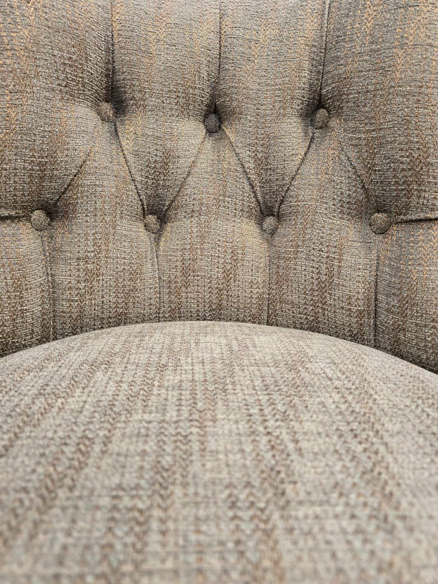 Close-up of beige and brown upholstered tufted armchair with button-tufted backrest.