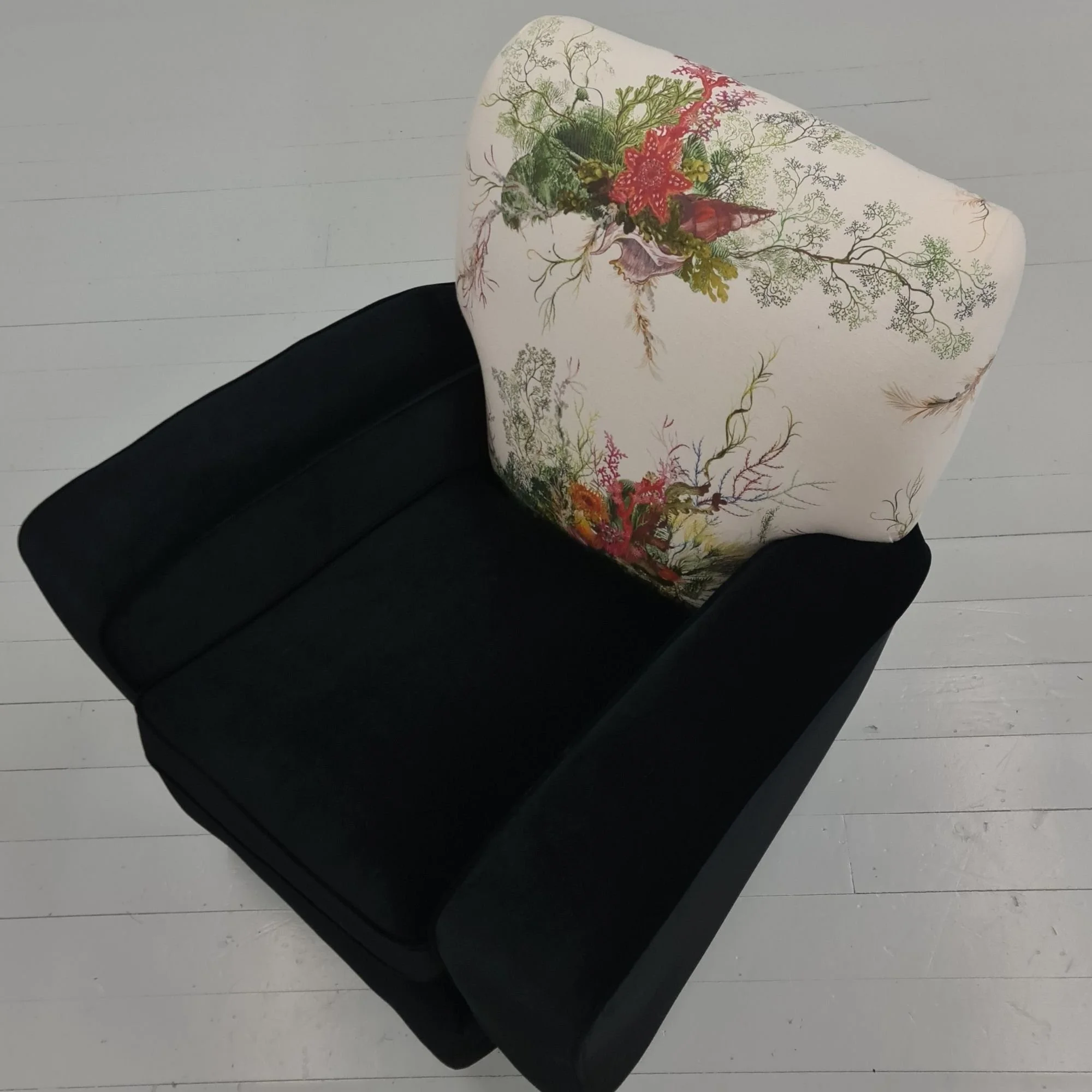 Black armchair with floral patterned cushion on white wooden floor.