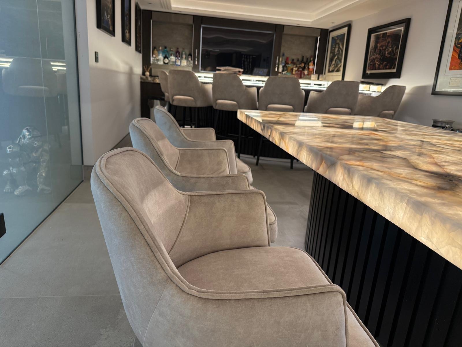 Bar area with beige armchairs arranged beside a marble countertop in a modern lounge.
