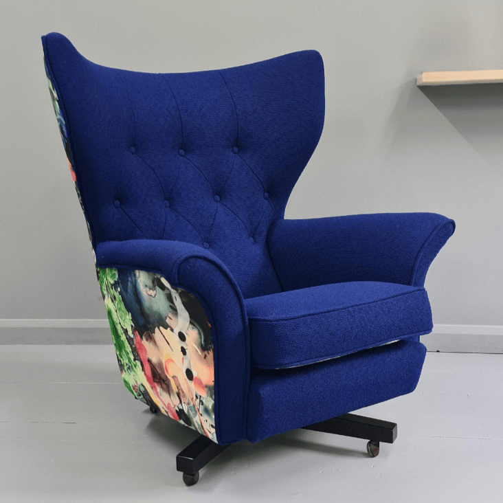 A blue upholstered armchair with floral-patterned sides, set on a gray floor against a plain gray wall.