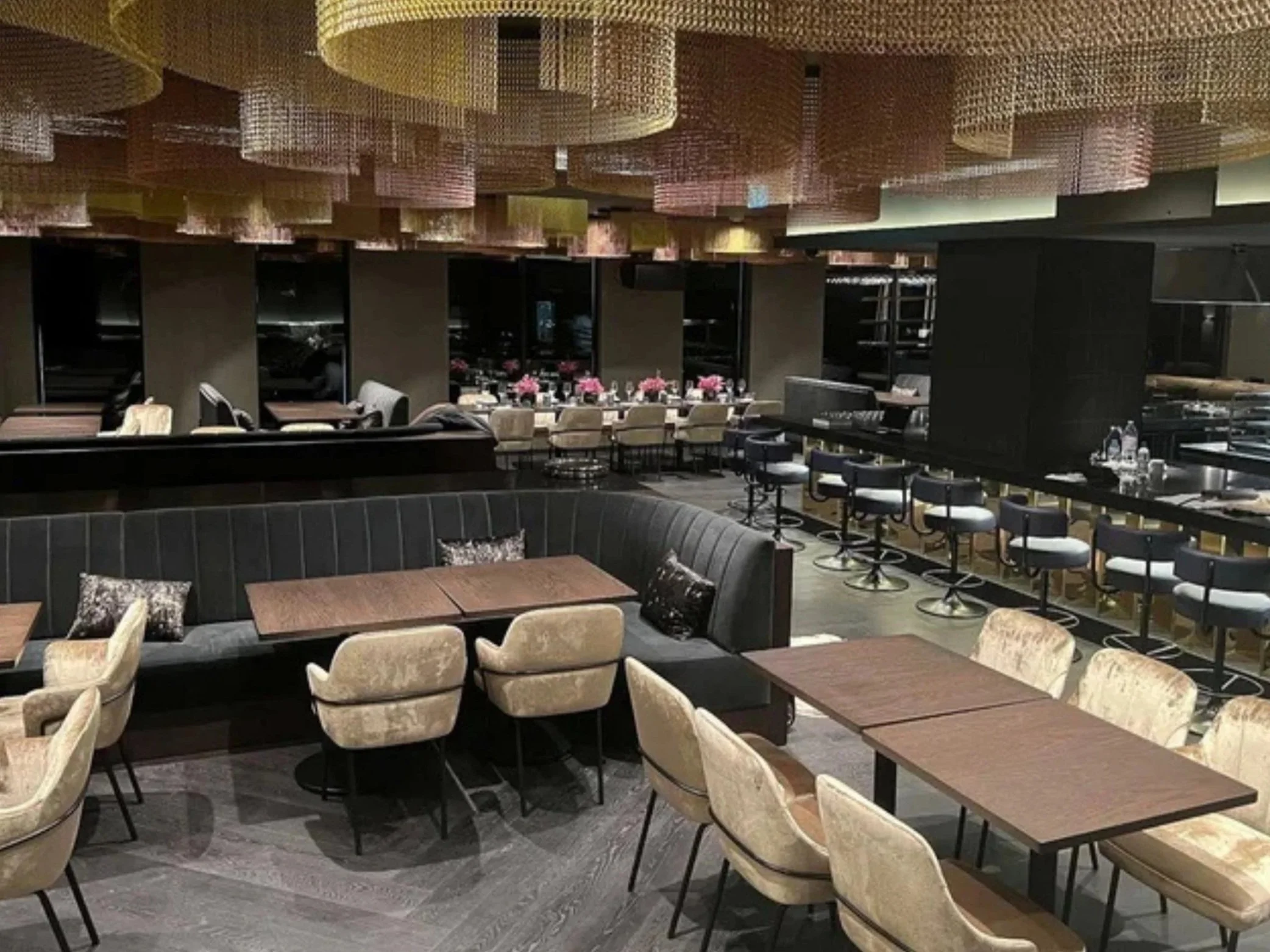 Interior of a modern restaurant with tables, chairs, and bar seating, decorated with pink flowers and intricate ceiling design.