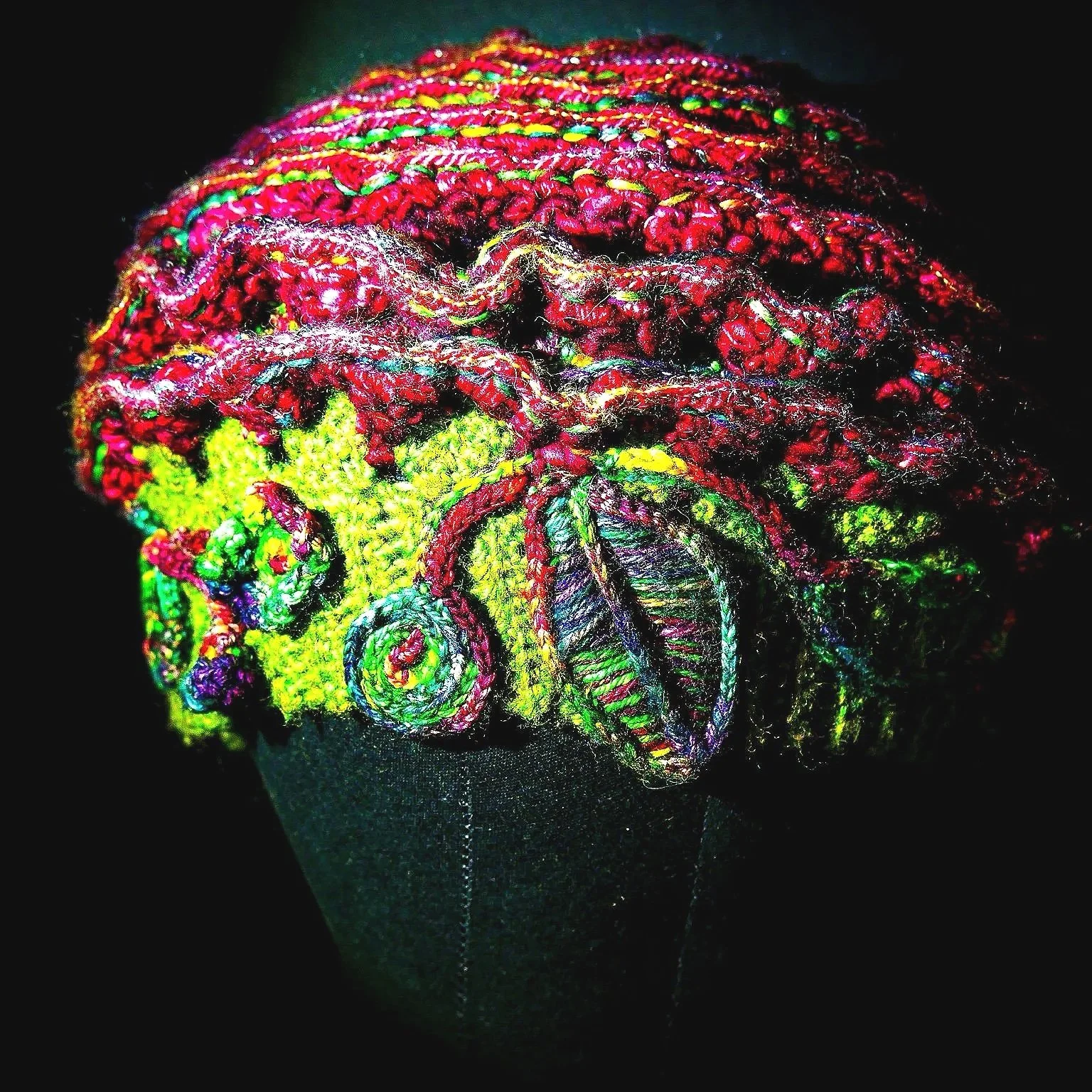 Front detail of The Cosmic Rose shows layered freeform crochet construction with a moss-green wool foundation and intricate silk-wool micro-stitching that creates prismatic color shifts.