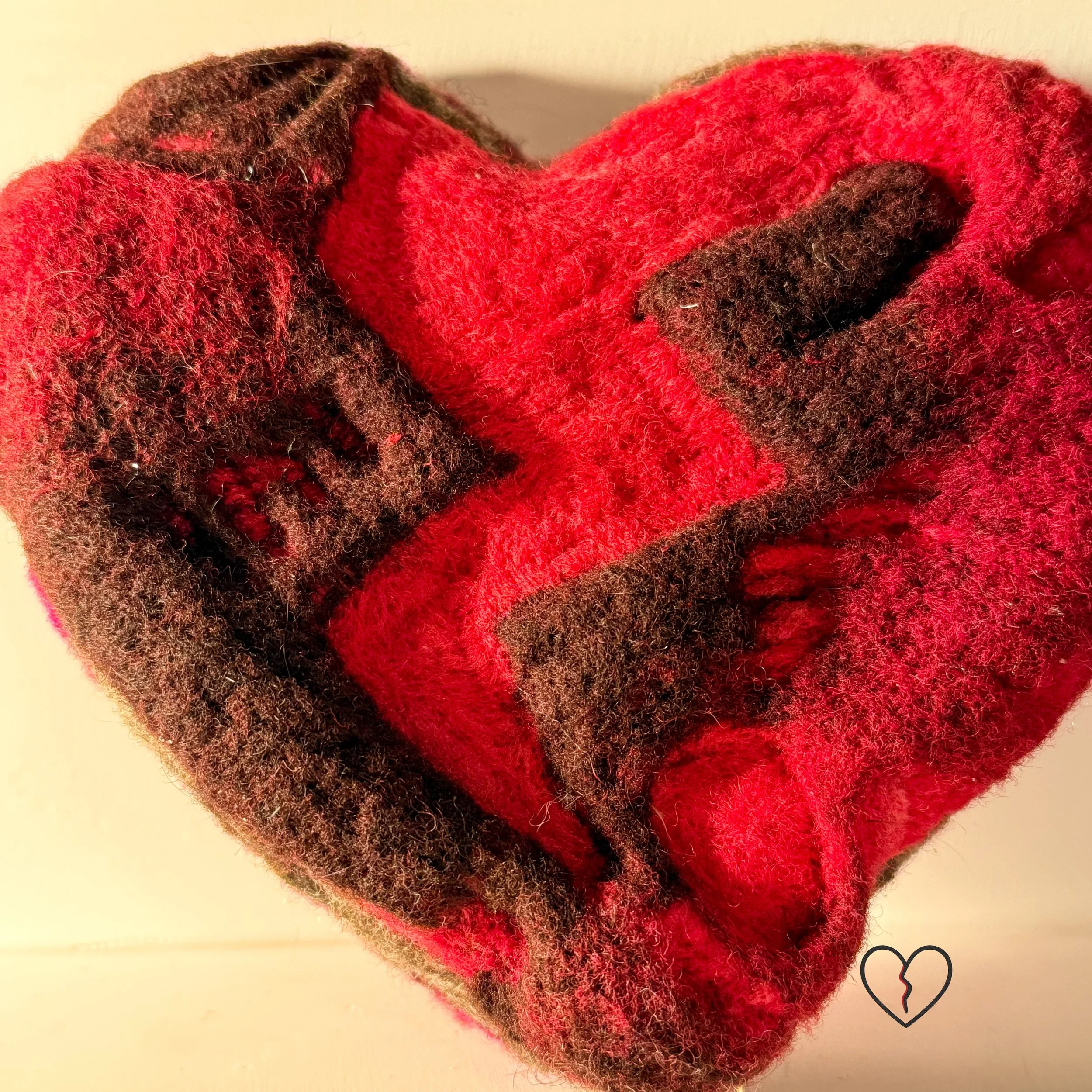 Close-up of needle-felted wool broken heart sculpture with molten red fibers flowing through a dramatic crack, soft texture visible