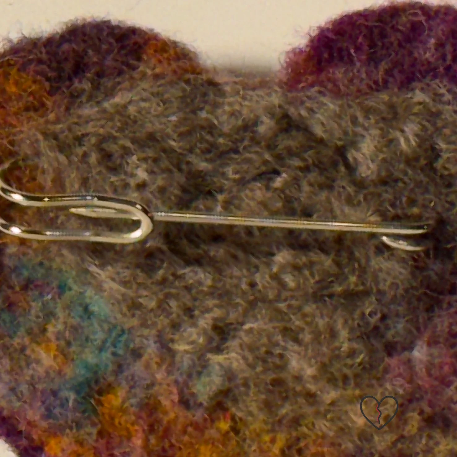 Needle-felted wool art pin broken heart with layered multicolored fibers and a stone-like texture, part of the Broken Heart series.