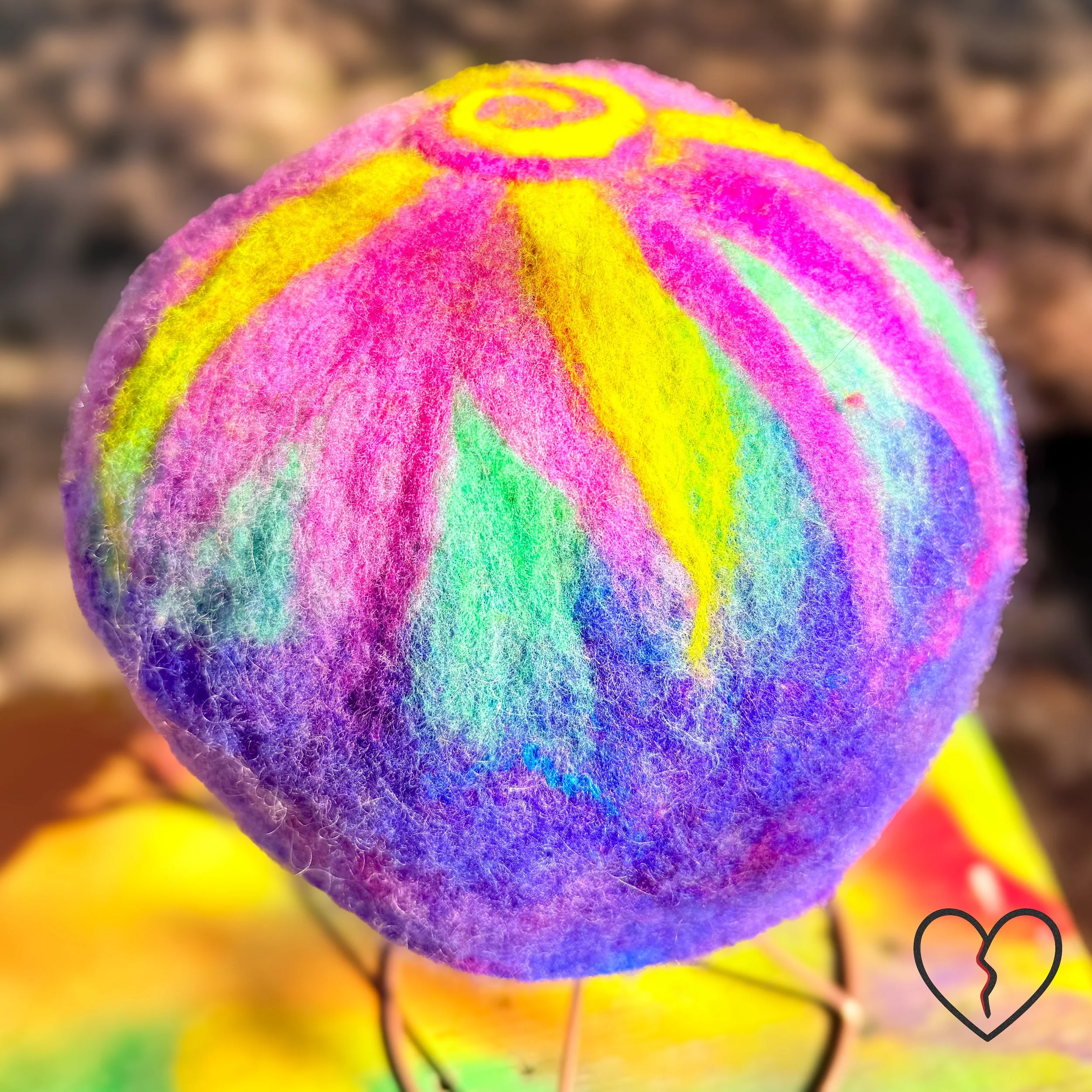 Hand dyed merino wool felted skullcap hat in purple, pink, and solar yellow with spiral sun symbol on crown