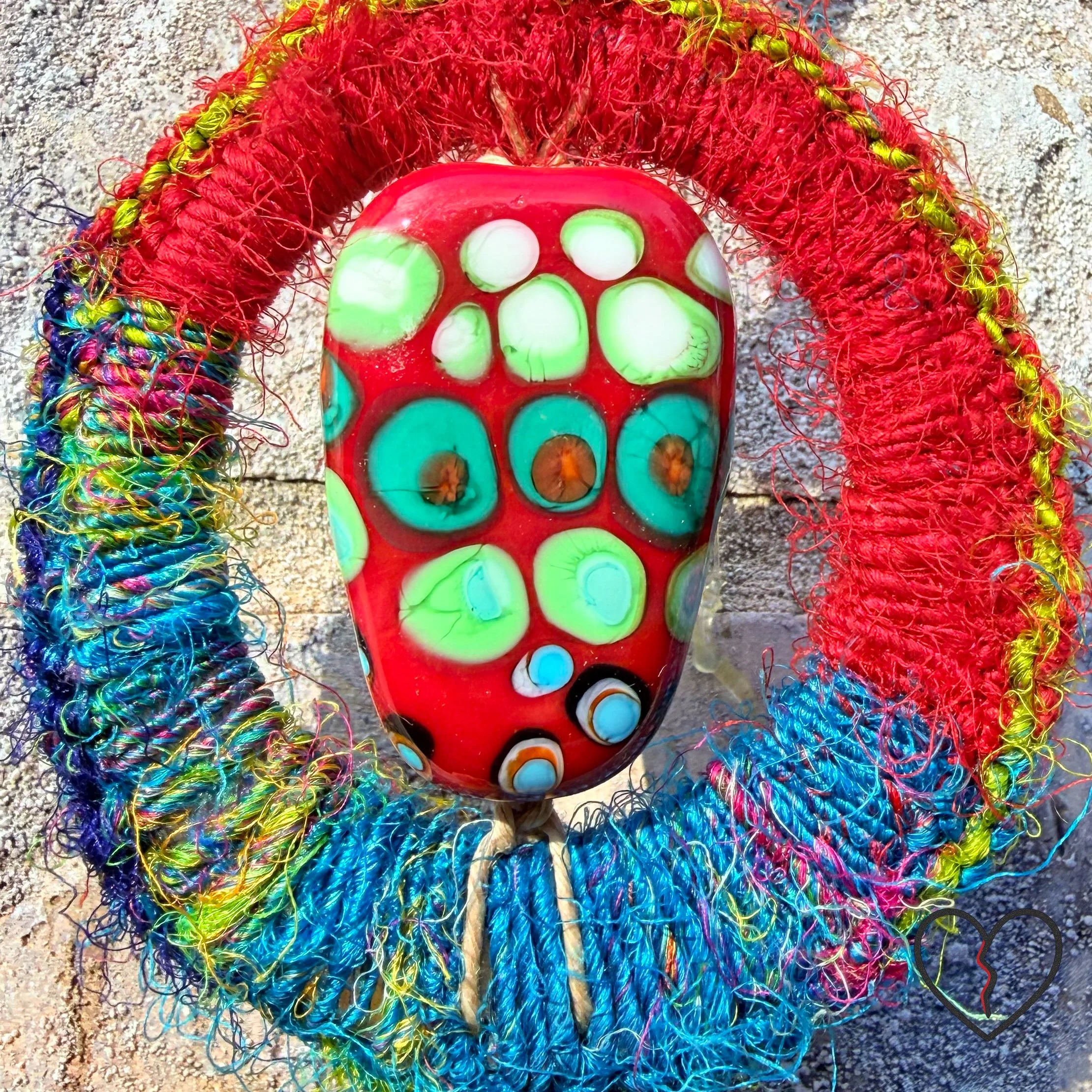 wrapped in sari silk crochet and hemp macrame with glass beads. The piece measures 11 inches long with a 2 inch largest ring and symbolizes triadic balance and transformation.