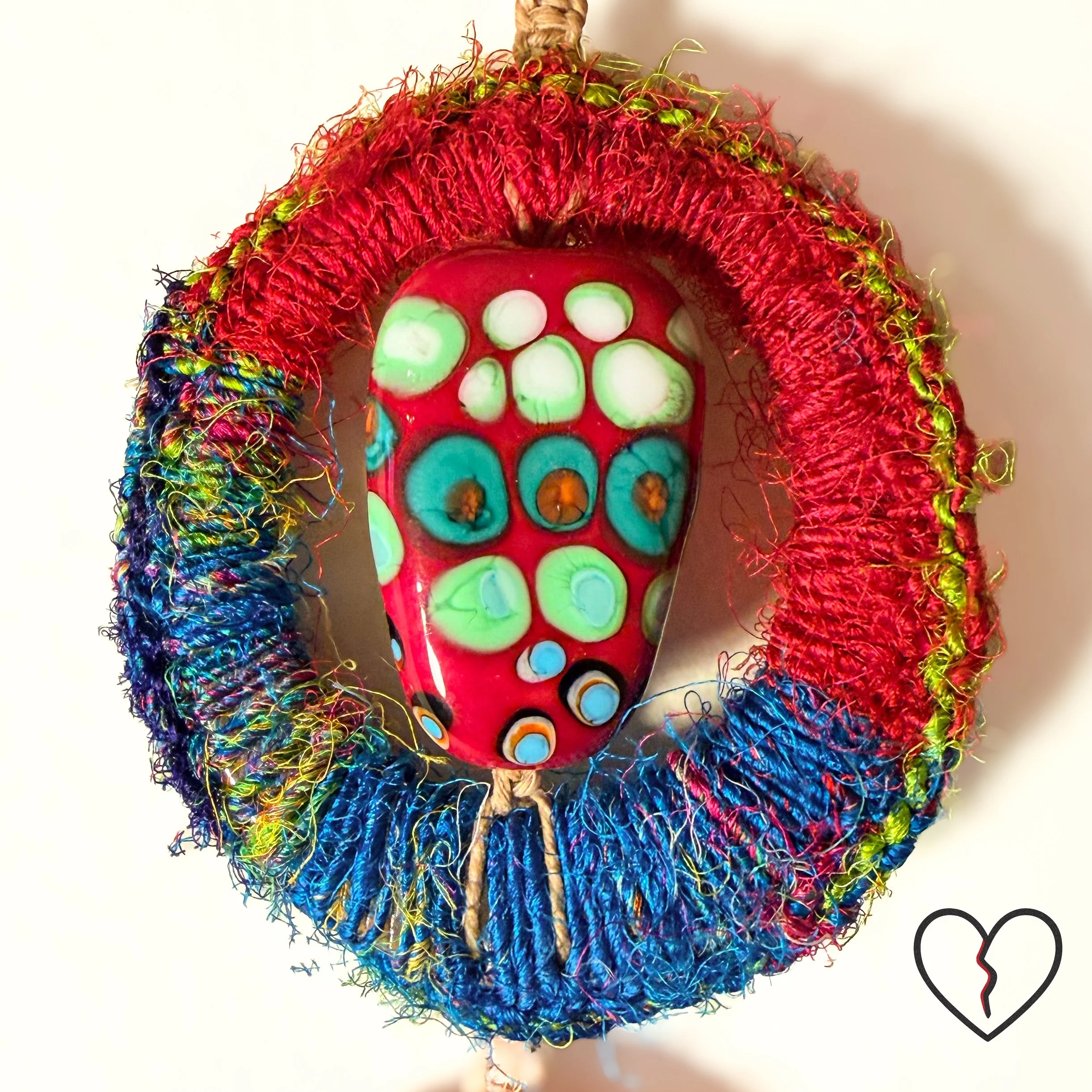 wrapped in sari silk crochet and hemp macrame with glass beads. The piece measures 11 inches long with a 2 inch largest ring and symbolizes triadic balance and transformation.