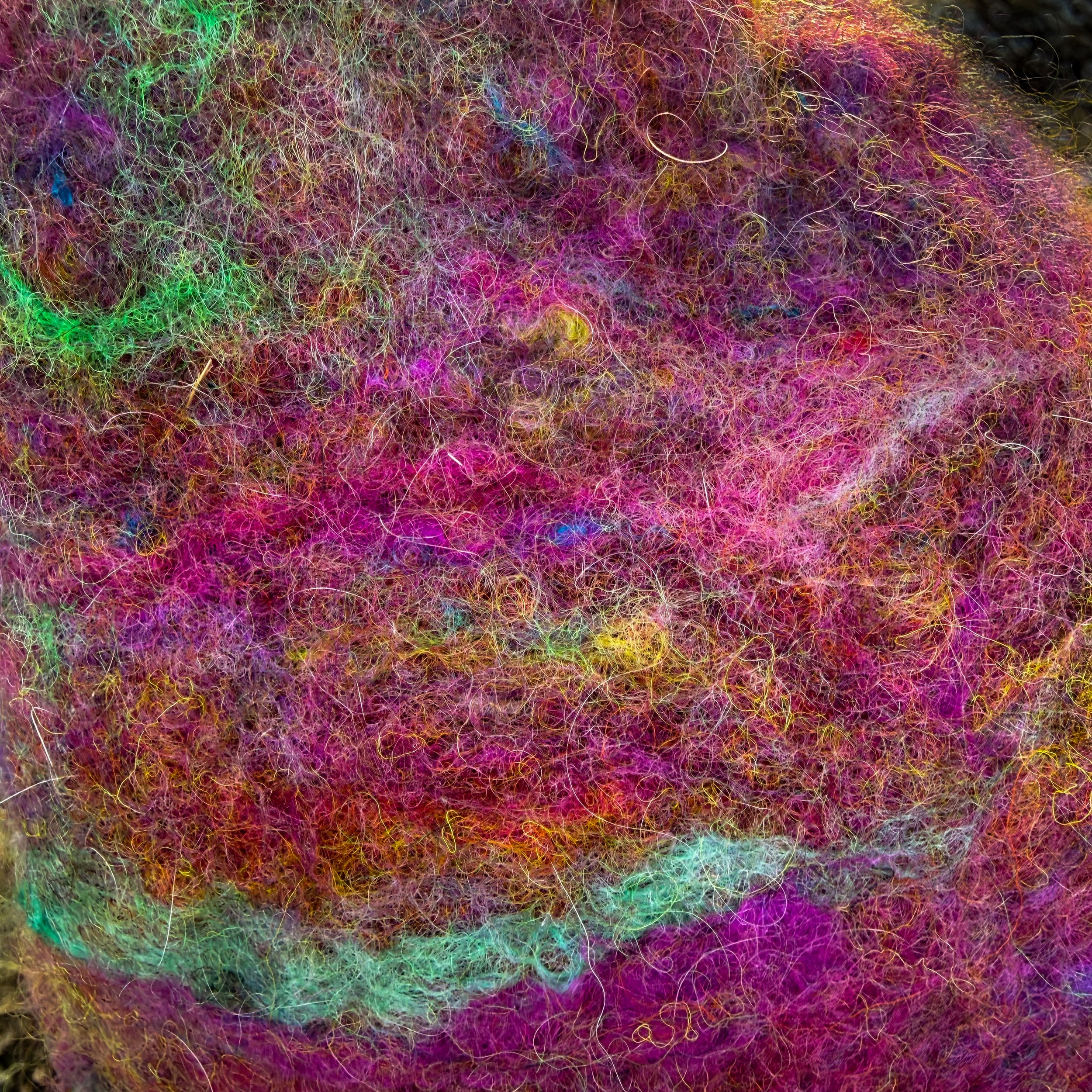 Detailed view of hand-felted wool fibers in pink, purple, green, and gold tones with visible silk and alpaca texture.