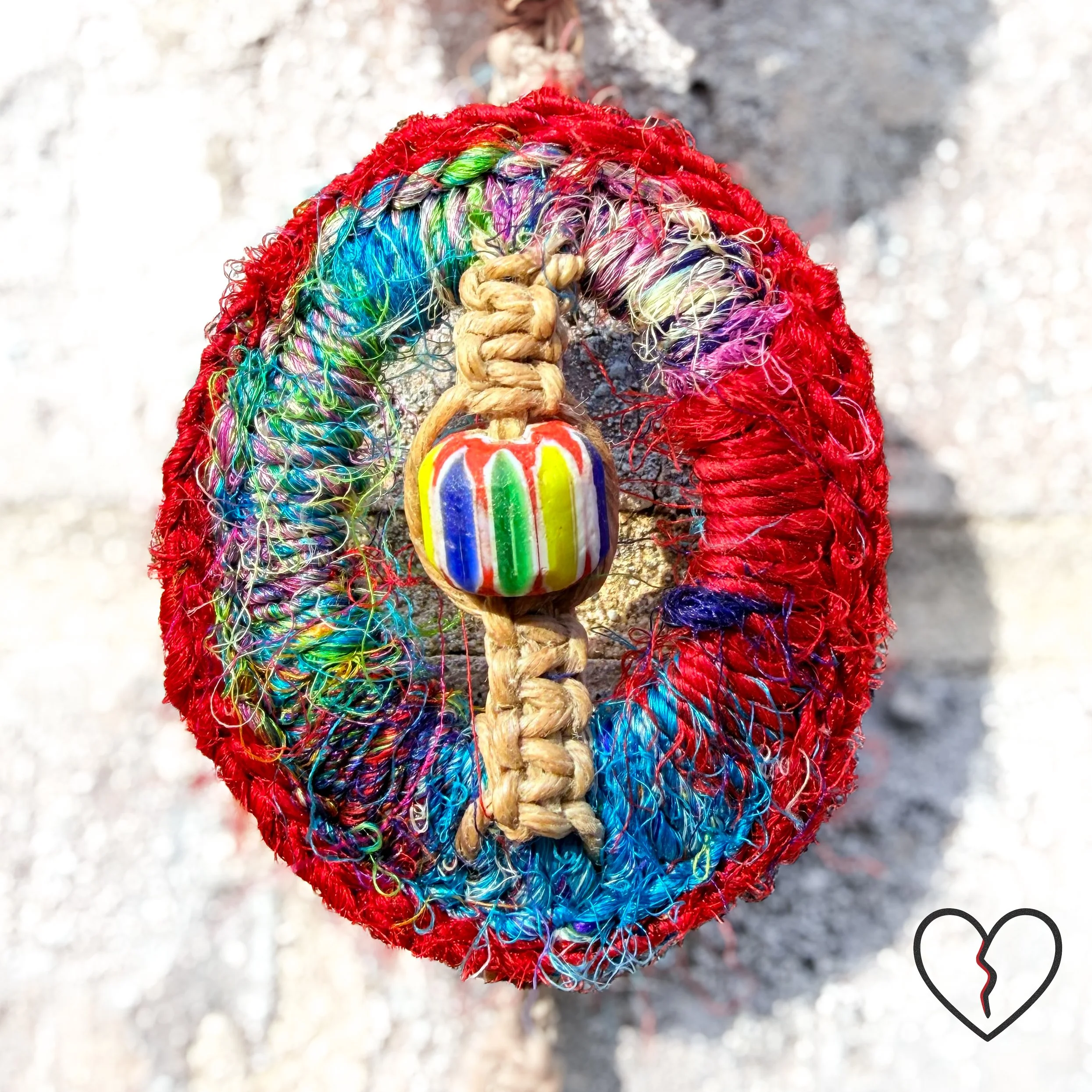 wrapped in sari silk crochet and hemp macrame with glass beads. The piece measures 11 inches long with a 2 inch largest ring and symbolizes triadic balance and transformation.