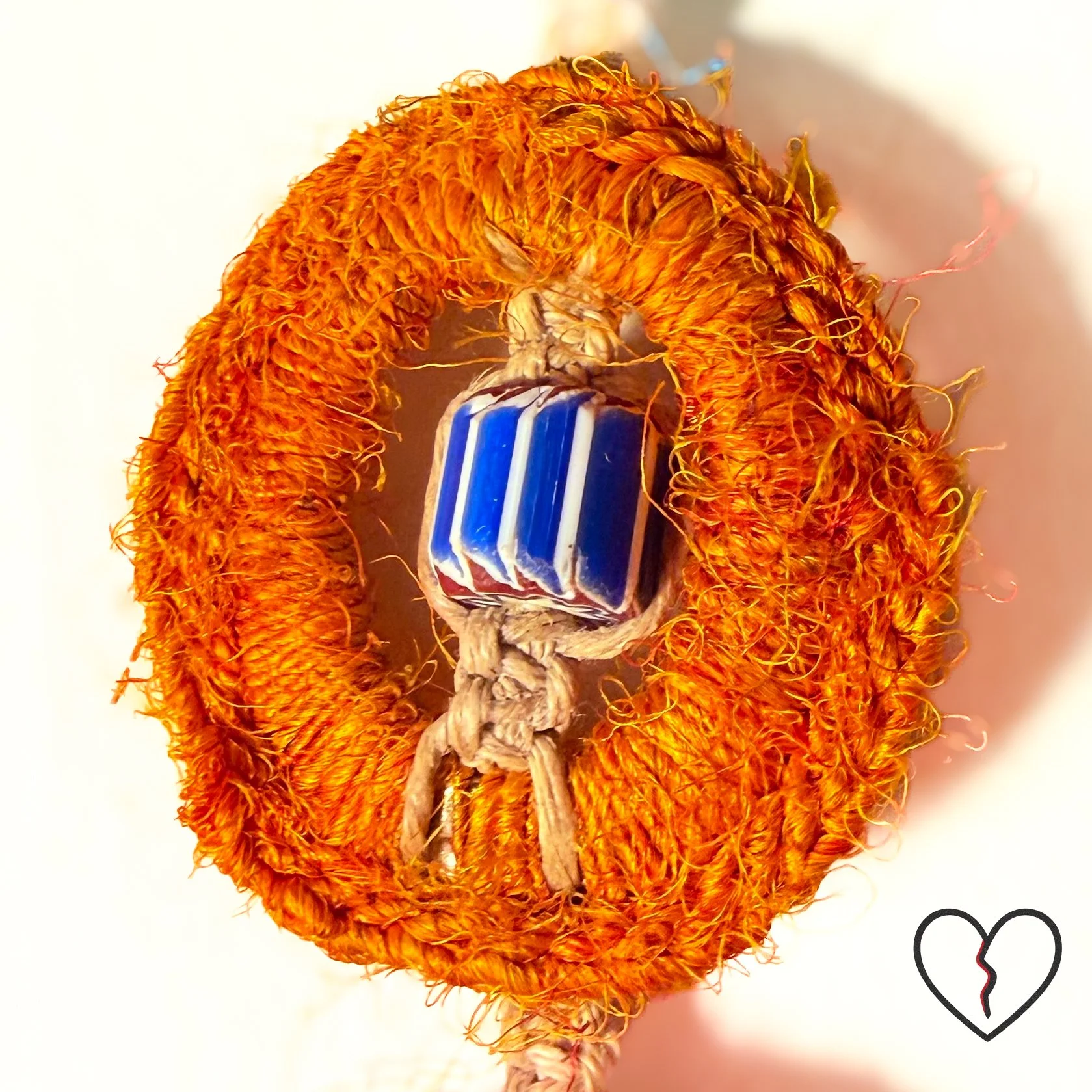 wrapped in sari silk crochet and hemp macrame with glass beads. The piece measures 11 inches long with a 2 inch largest ring and symbolizes triadic balance and transformation.