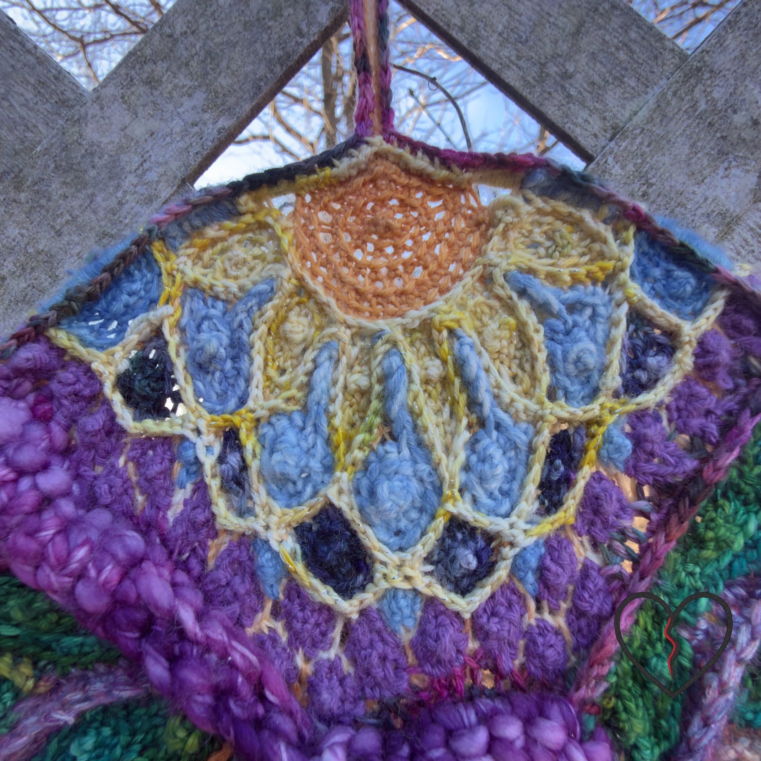 Close-up of textured crochet stitches in purple and blue wool forming layered, interconnected shapes in a symbolic fiber wall hanging.