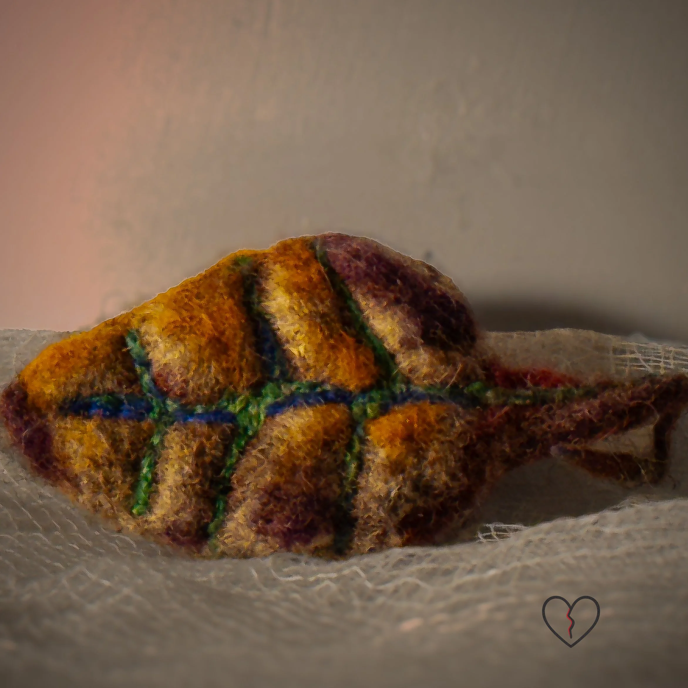 Needle felted wool leaf pin in warm autumn colors of yellow, purple, and earthy tones, photographed on soft white fabric with jewelry pin backing.