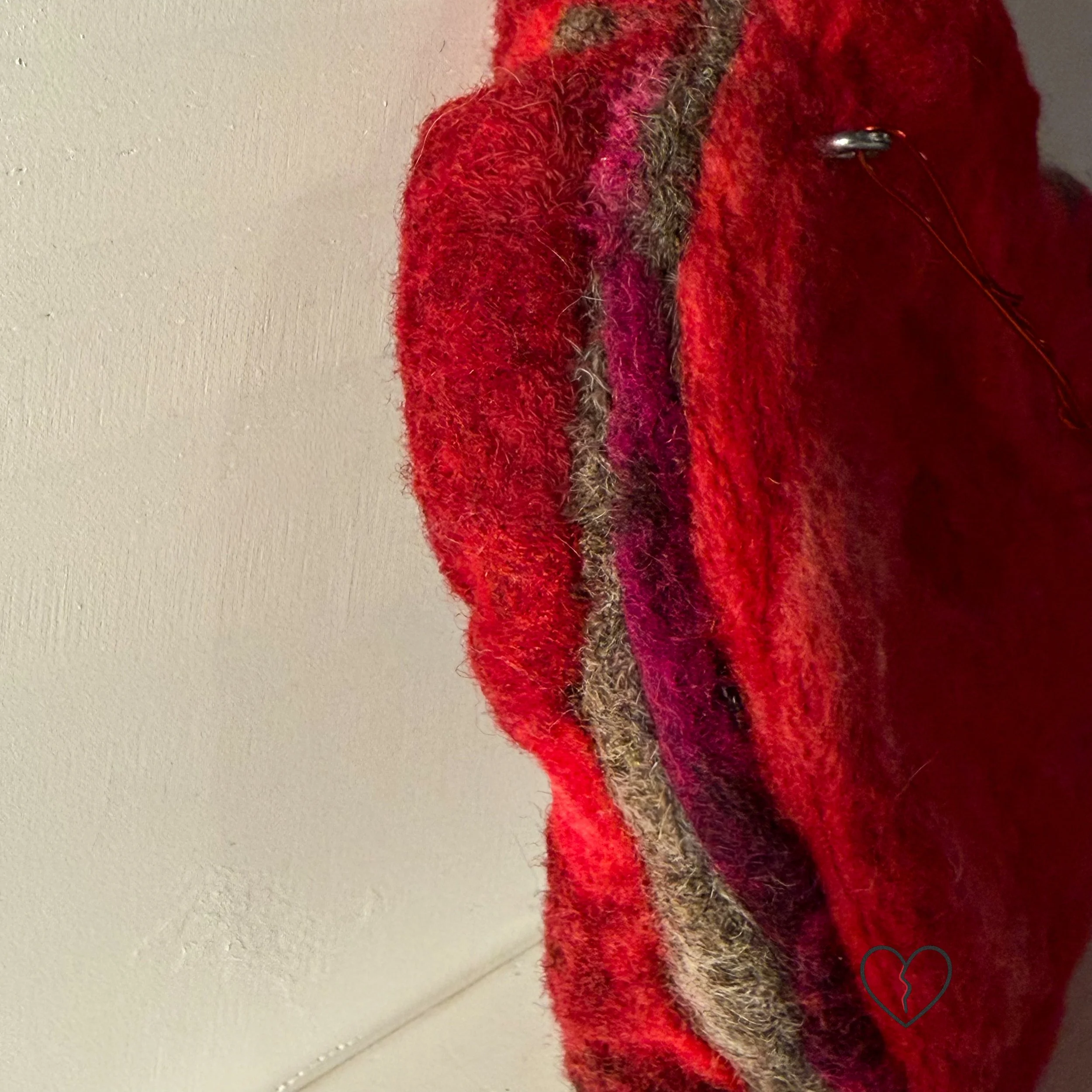 Edge detail of needle-felted wool broken heart artwork revealing stacked layers of hand-dyed wool fibers