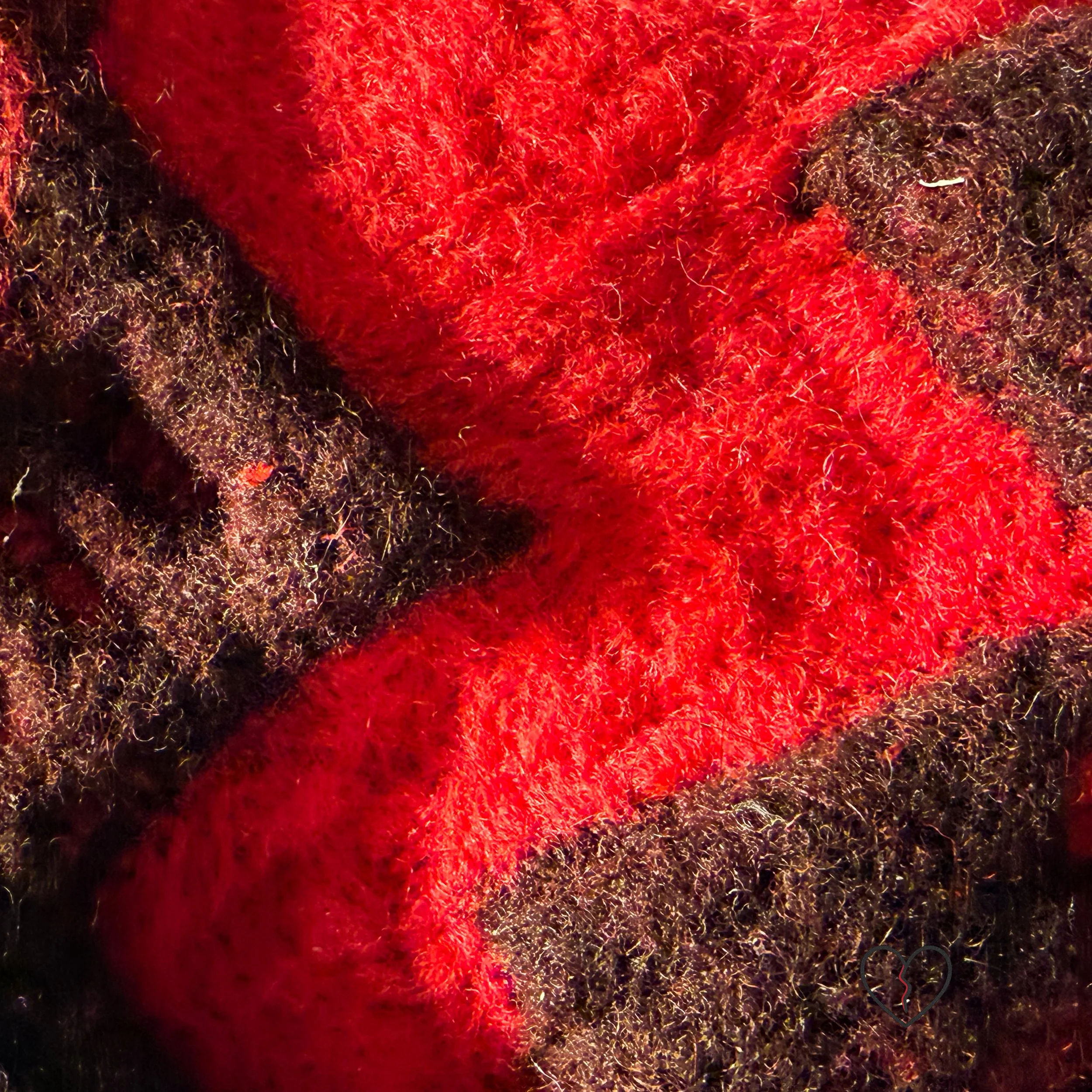 Detail of red and dark brown needle-felted wool showing layered fibers and volcanic texture in broken heart wall art