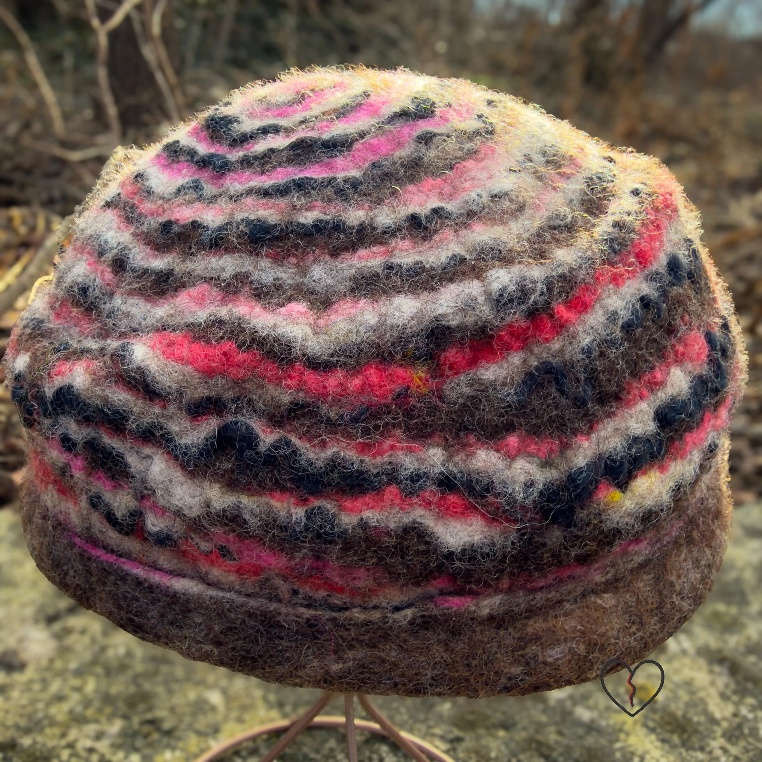 Angled back view of a sculptural wool hat showing wave-like felted stripes and a folded brim, emphasizing texture and hand-shaped form.