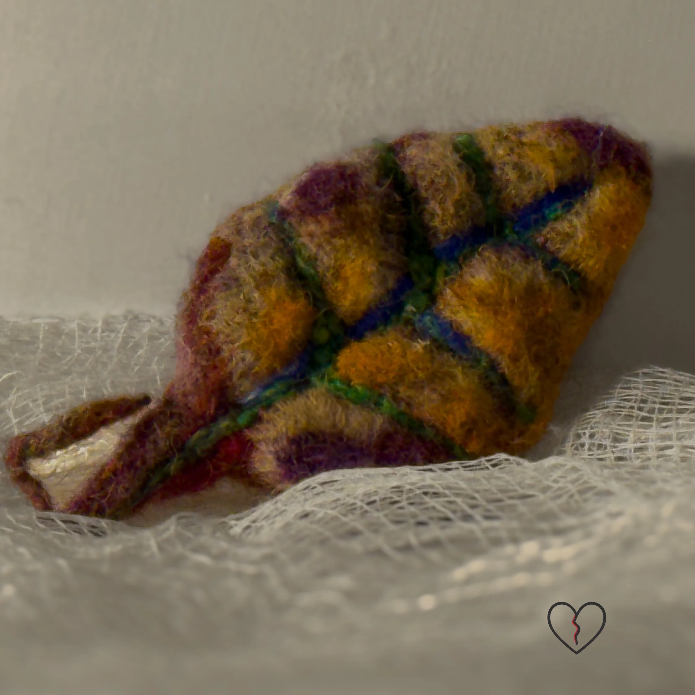 Needle felted wool leaf pin in warm autumn colors of yellow, purple, and earthy tones, photographed on soft white fabric with jewelry pin backing.