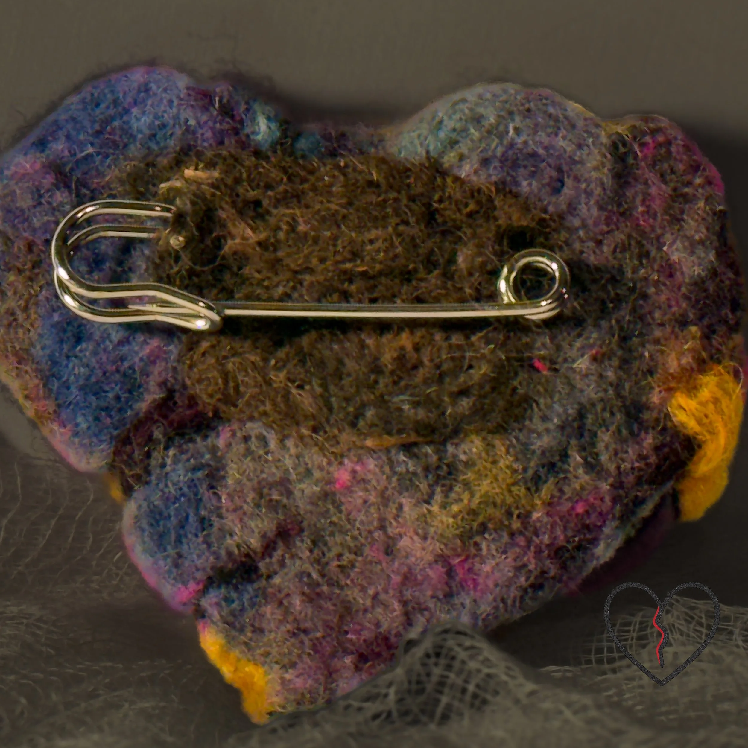 Angled close-up highlighting dimensional relief and sculptural depth of a wool broken heart pin.