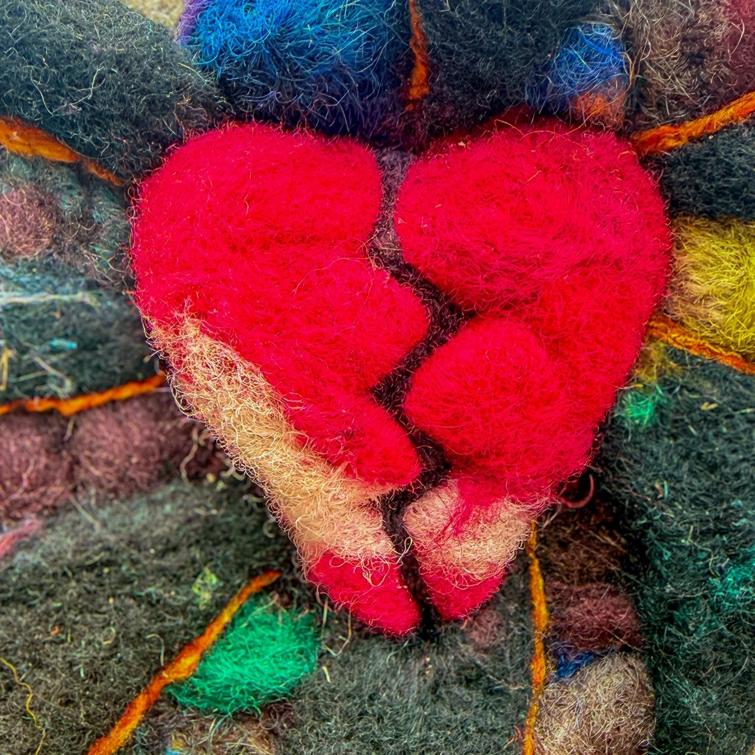 Close-up of a red split heart needle-felted in wool.