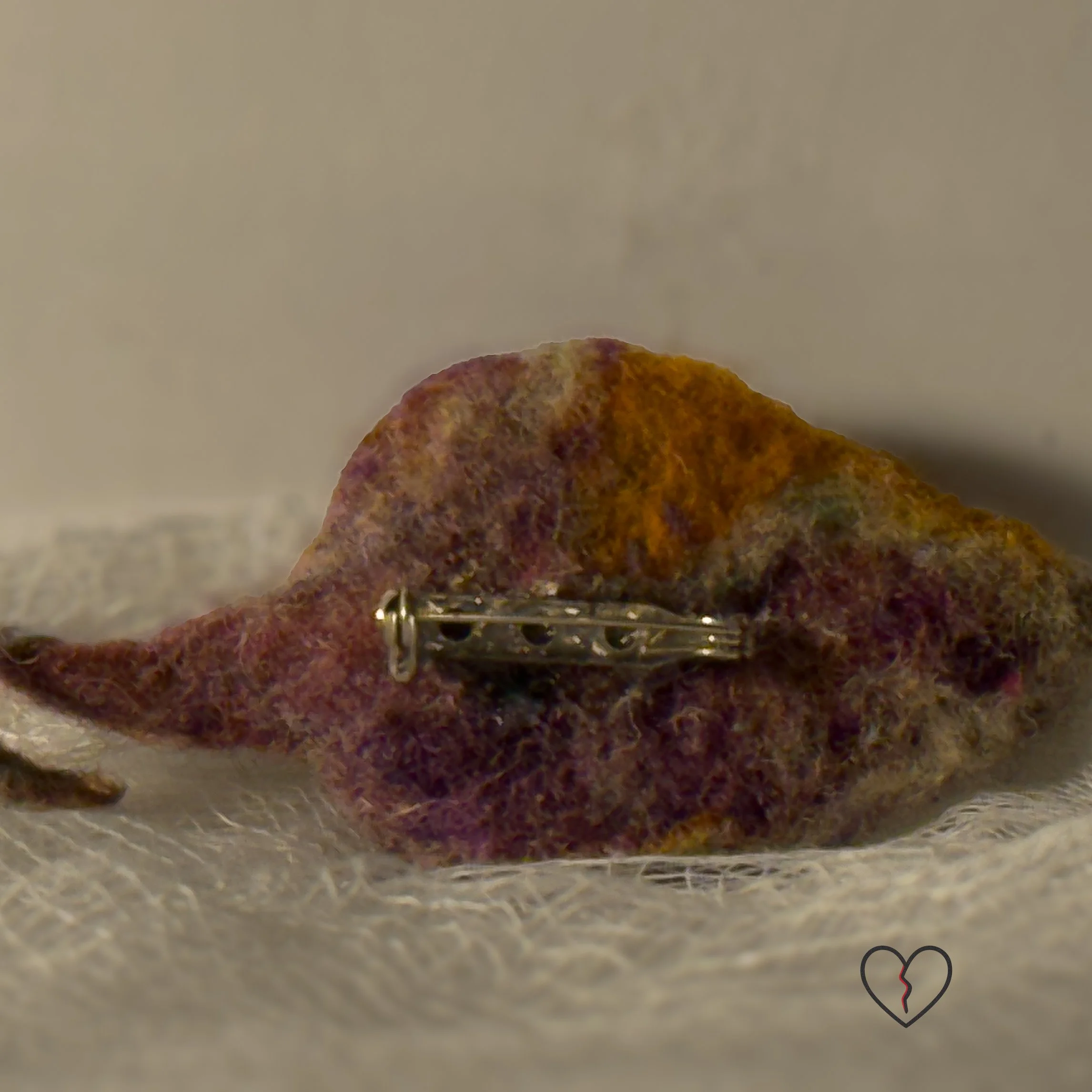 Needle felted wool leaf pin in warm autumn colors of yellow, purple, and earthy tones, photographed on soft white fabric with jewelry pin backing.