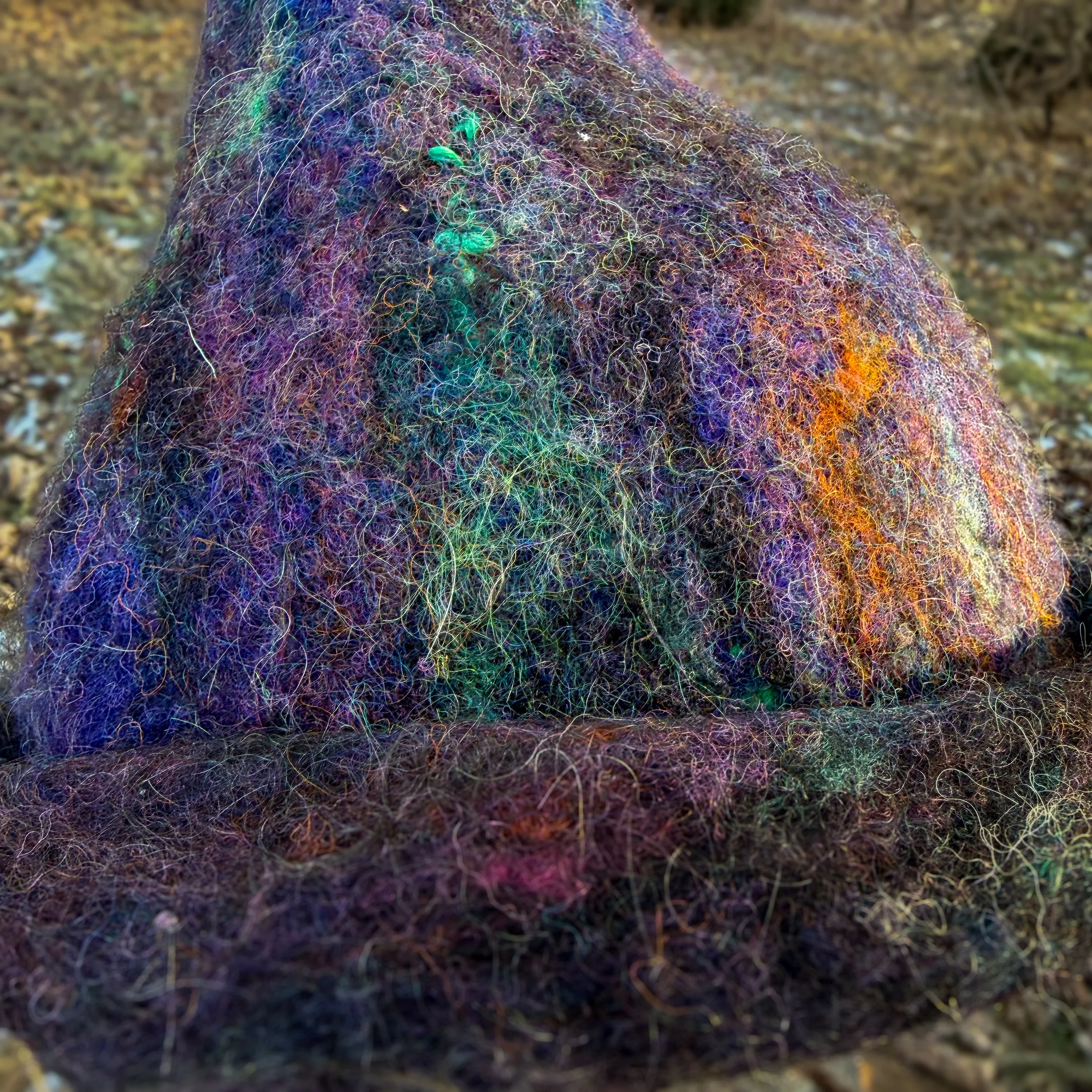 Close-up of a hand-felted purple and black wool witch hat showing layered fibers and subtle color variation.