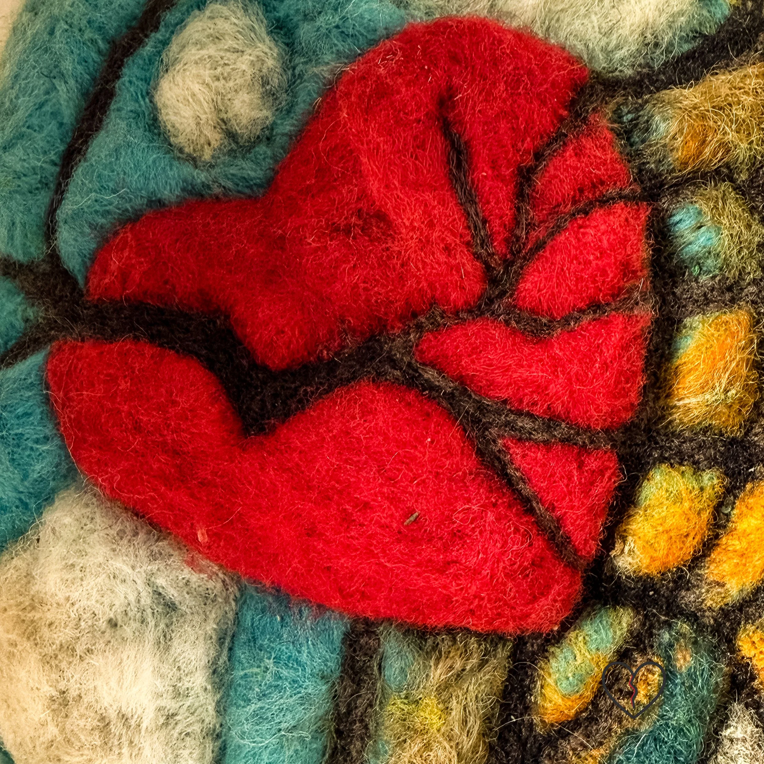 Close-up of broken red heart in needle felted wool artwork Fractured Landscape, showing cracks spreading outward.