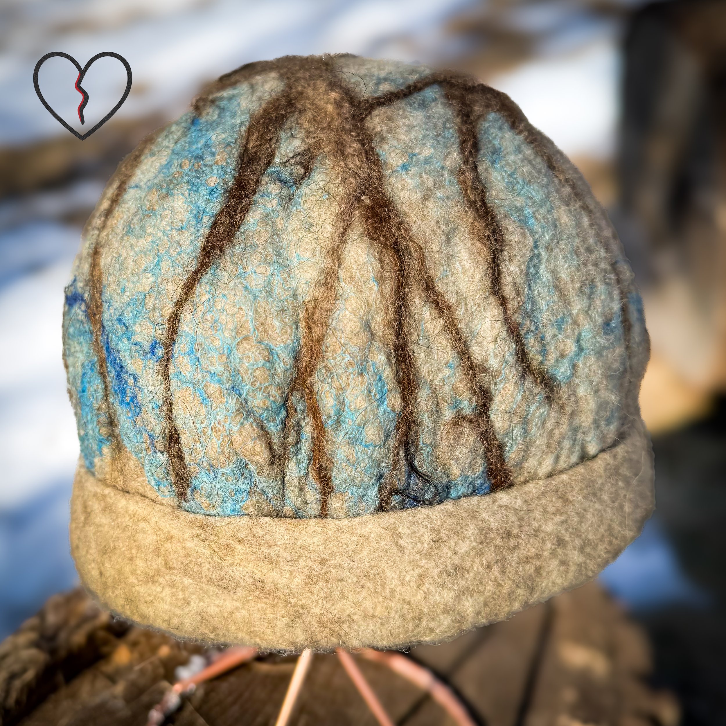 Front angle of wet felted wool hat with folded natural brown brim and branching tree across blue silk sky, Grounded Thought wearable fiber art