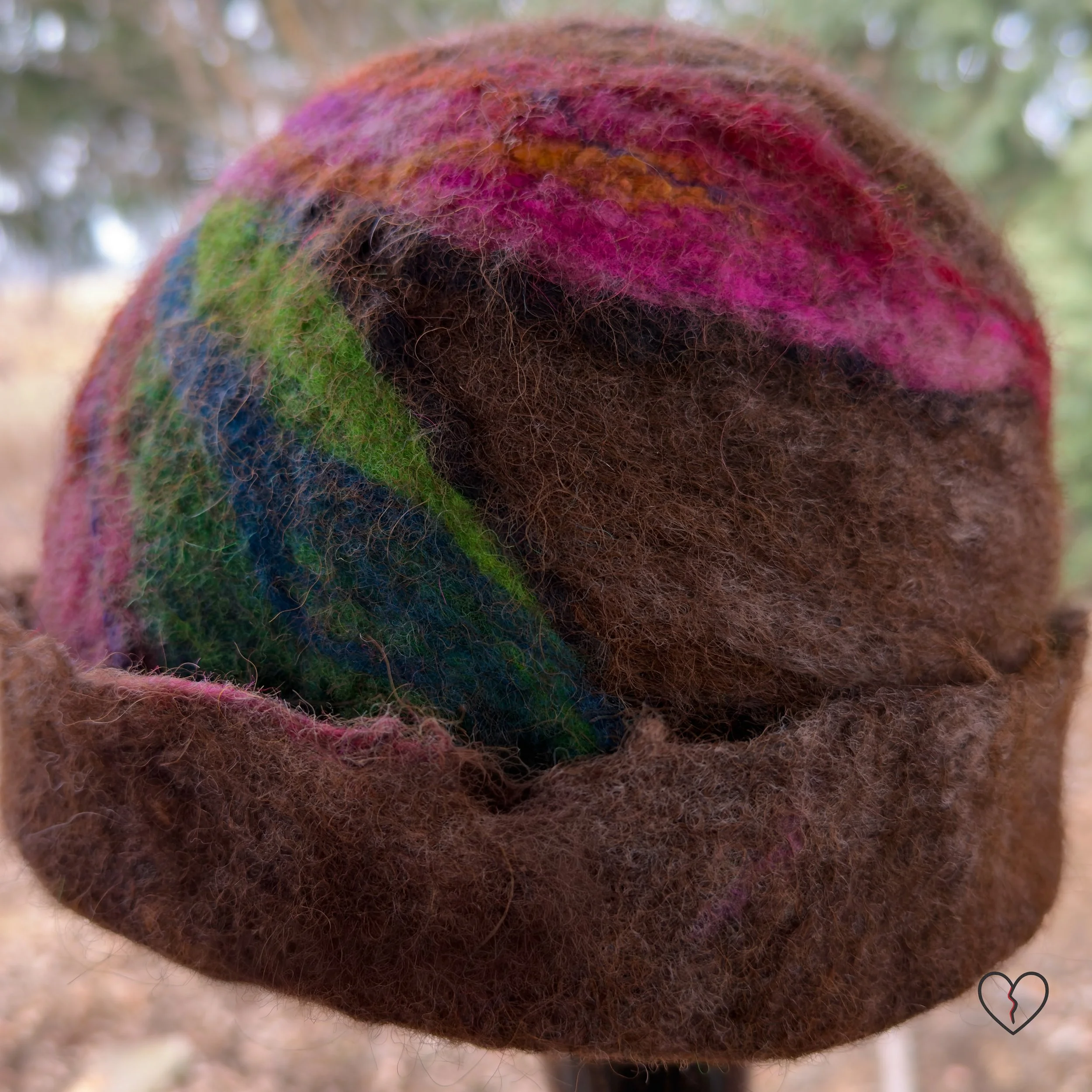 Side view of sculptural wool hat with folded brown brim and pink accents