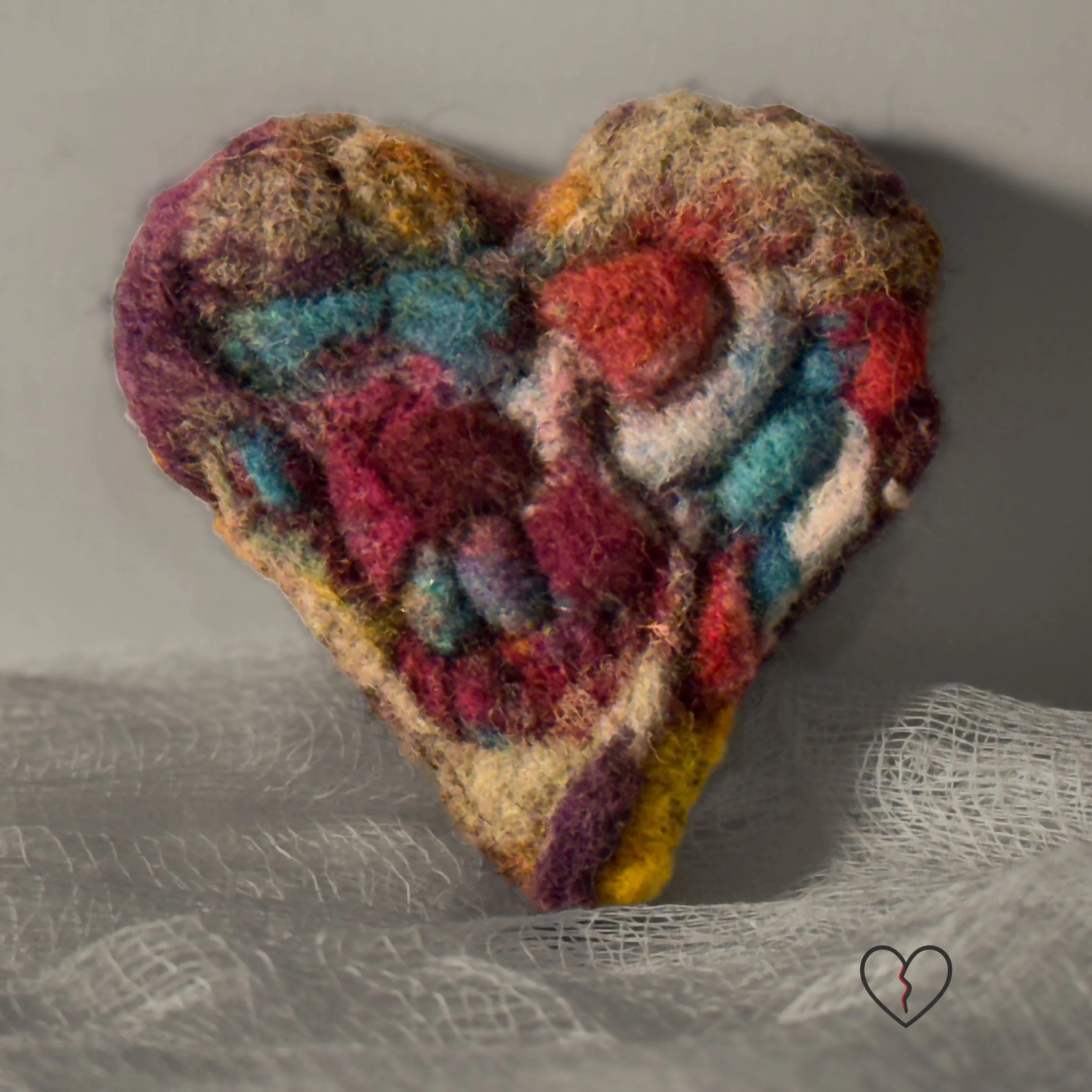 Needle-felted wool art pin broken heart with layered multicolored fibers and a stone-like texture, part of the Broken Heart series.