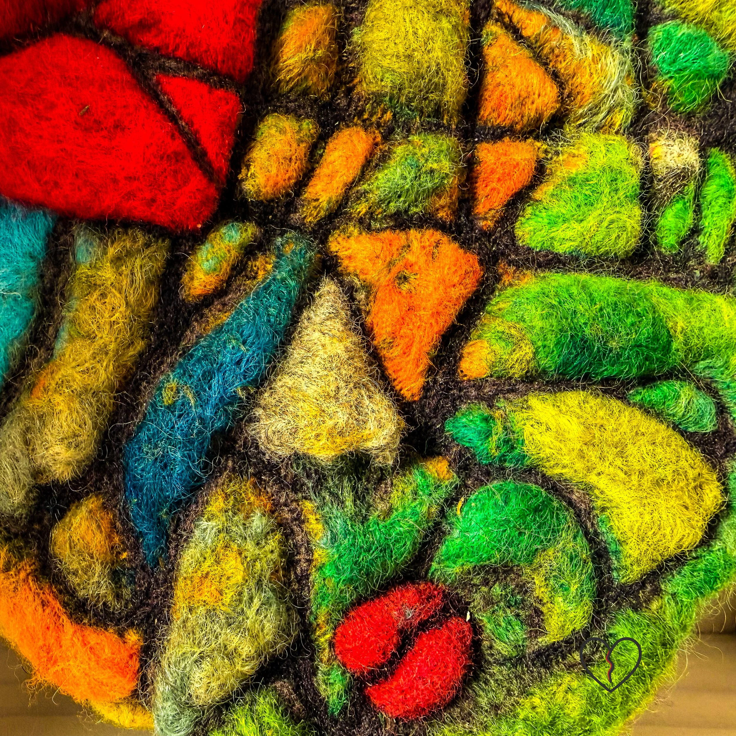 Detail of fractured land in needle felted wool wall art Fractured Landscape with green, yellow, and orange mosaic-like sections.