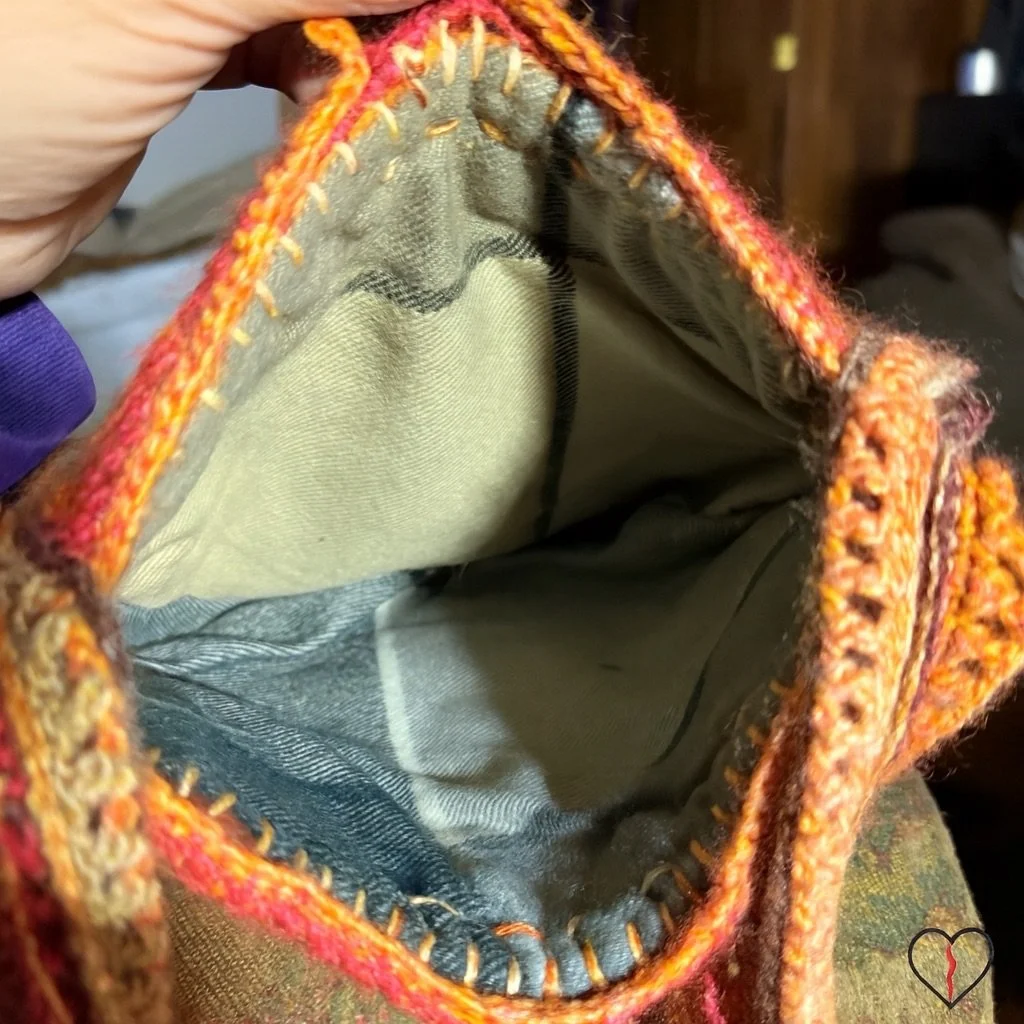Interior view of a handmade wool purse showing hand-sewn fabric lining, visible embroidery stitches, and crocheted edging attached by hand.