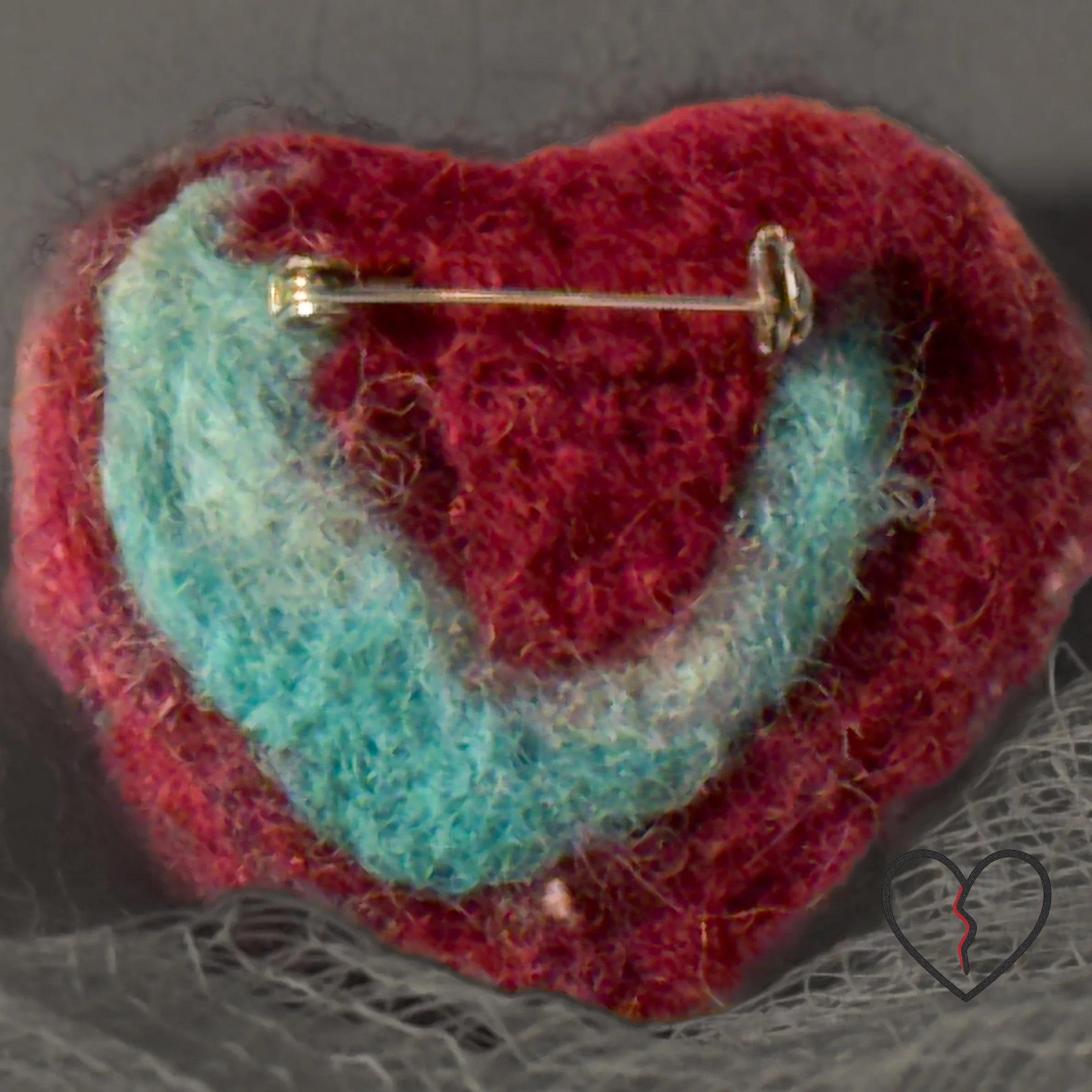 A tiny hand-felted broken heart pin made from hand-dyed purple merino wool with a soft pink wisp. Lightweight, hopeful fiber art by Kristi Yapp – Wool Alchemist.