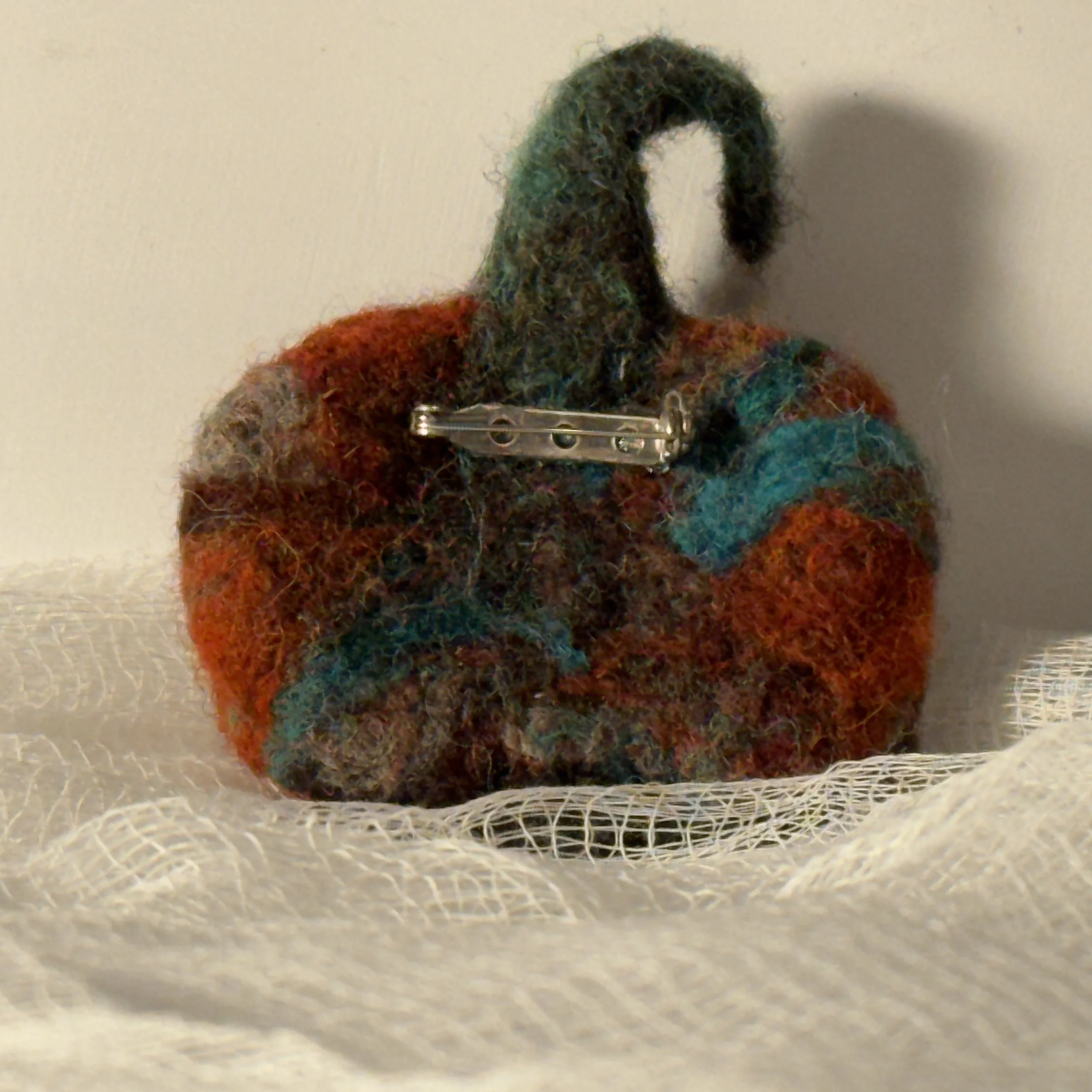 A group of handmade needle felted wool art pins, each one of a kind, showing organic shapes, soft sculptural texture, and layered wool fibers in muted seasonal tones.