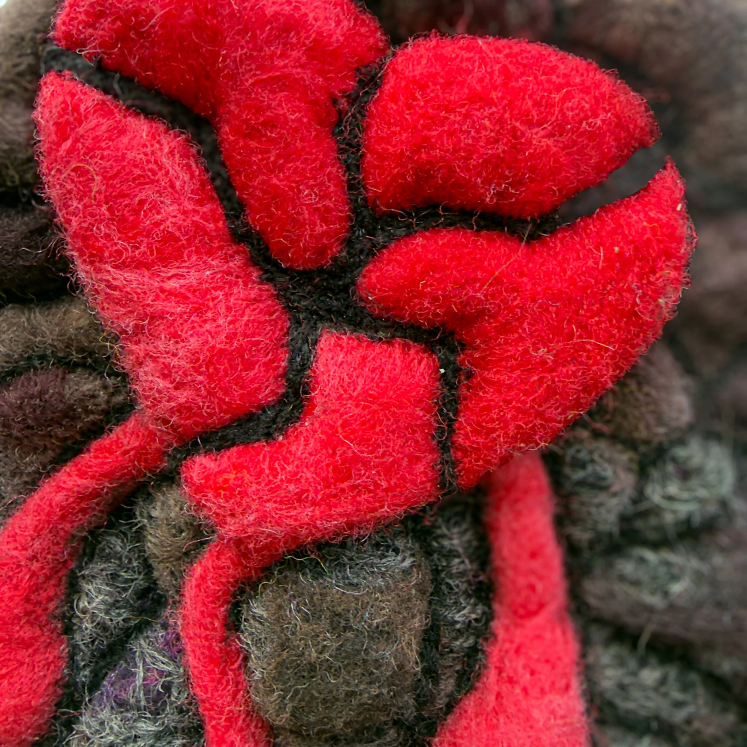Detail view of dripping red felt scars against mottled gray and brown wool texture