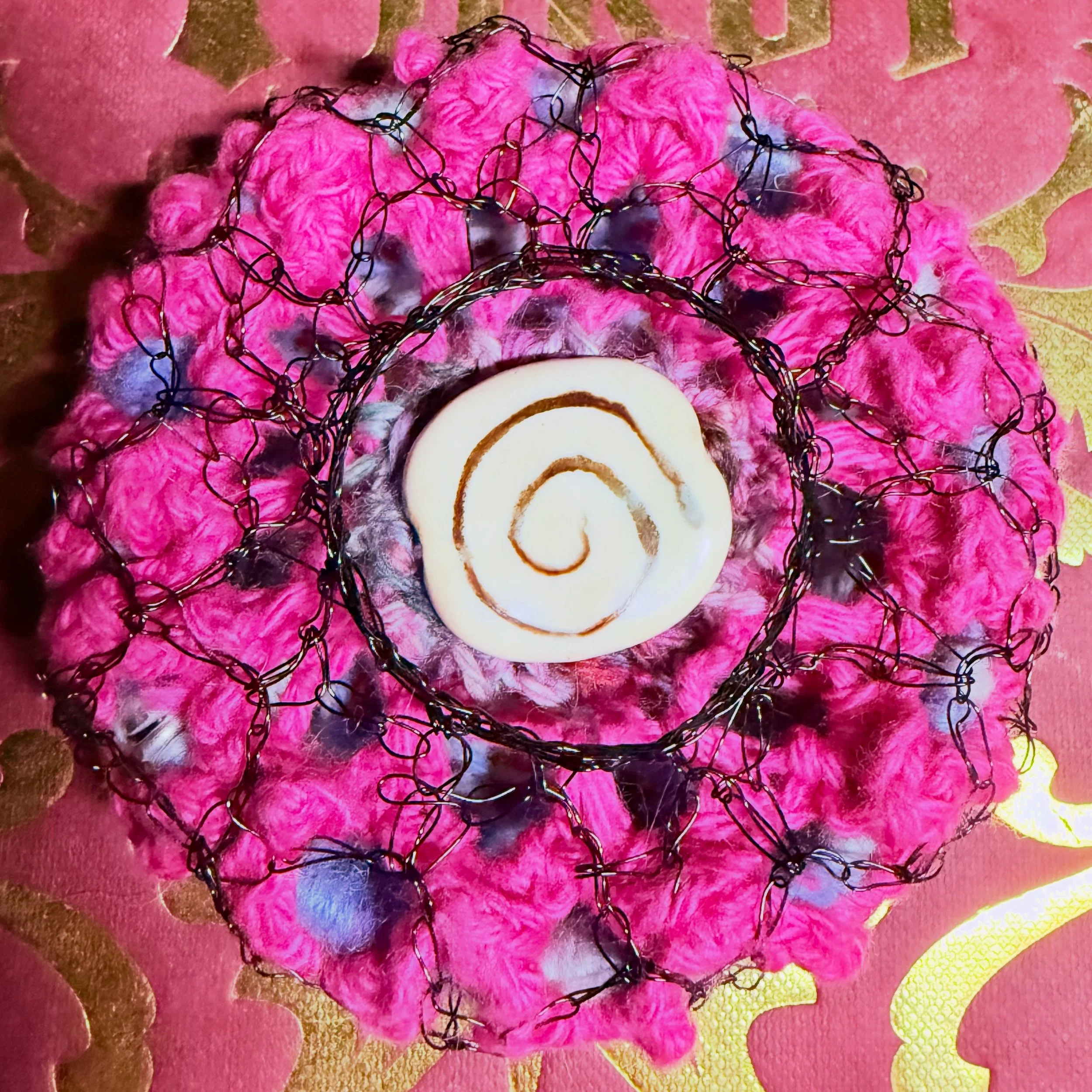 Handmade spiral talisman art pin crocheted with wool, cotton, and black wire around a repurposed bracelet base.