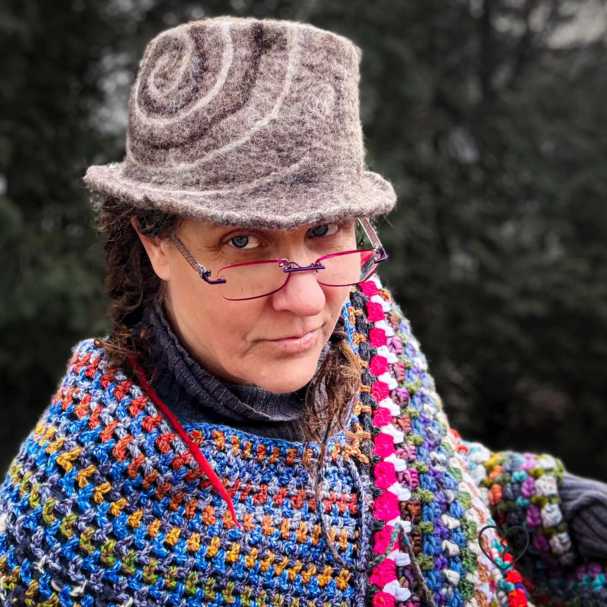 Hand-felted wool fedora hat in natural brown tones with a white and dark brown spiral design, sculptural crown, and short brim, photographed outdoors.