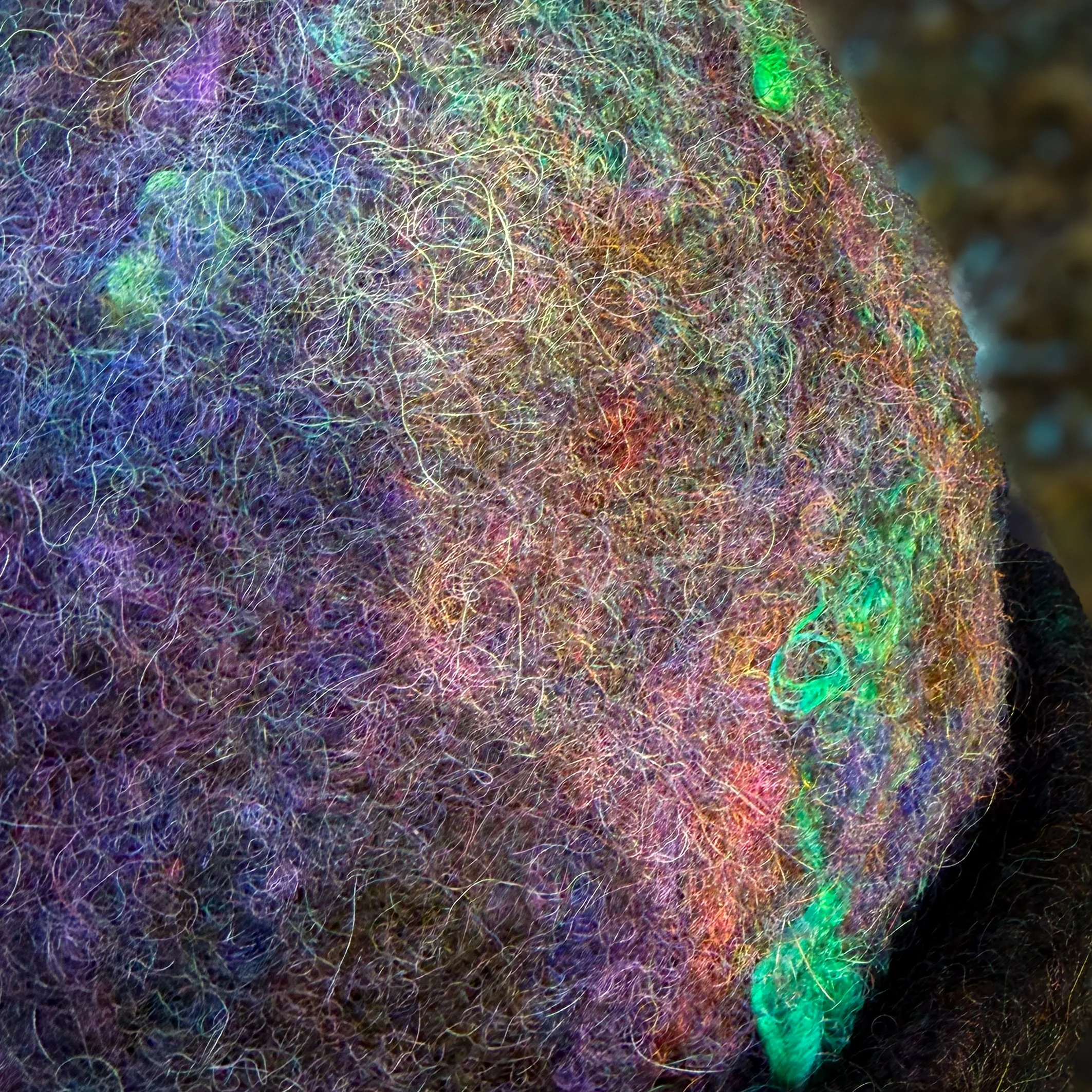 Detailed view of hand-felted wool fibers in purple, black, teal, and gold tones with visible silk texture.