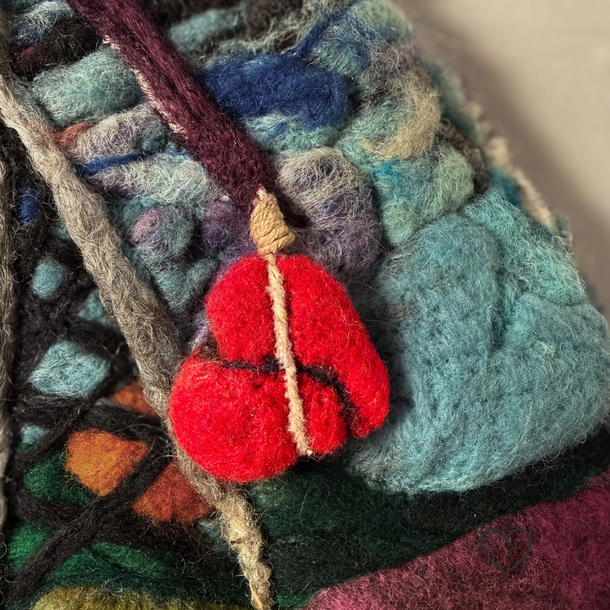 Needle felted wool wall art showing a rural landscape disrupted by a cell tower with a red broken heart hanging beneath it.