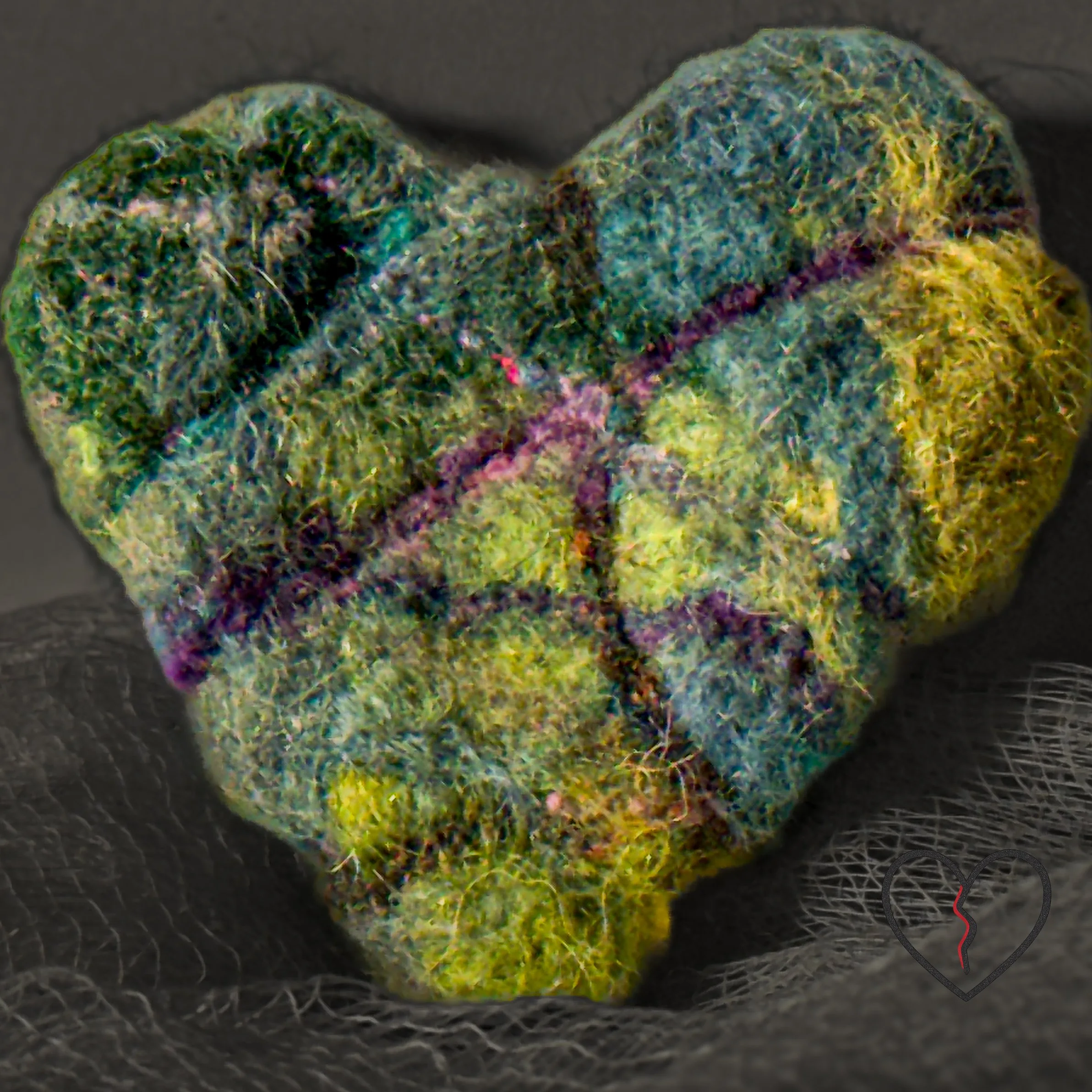 Hand-felted broken heart pin in moss green wool with purple veins running through surface cracks, shown front view