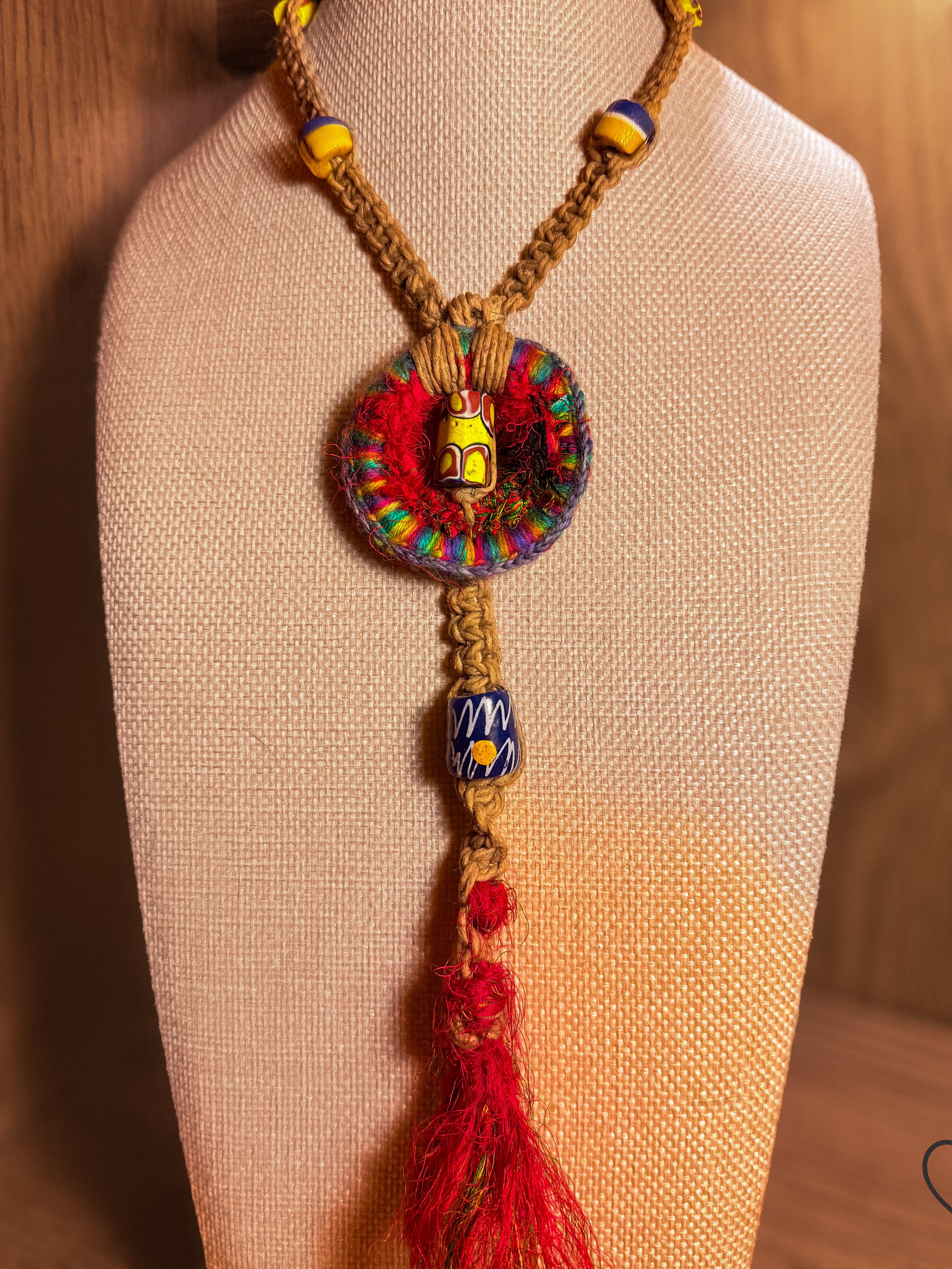 Fiber necklace with yellow trade bead, wool circle, hemp cord, and tassel.